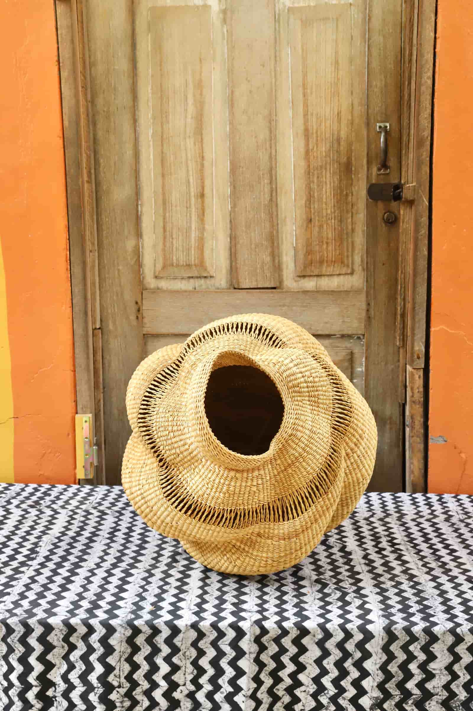 Woven conch on a black and white patterned tablecloth in front of a wooden door with orange wall.