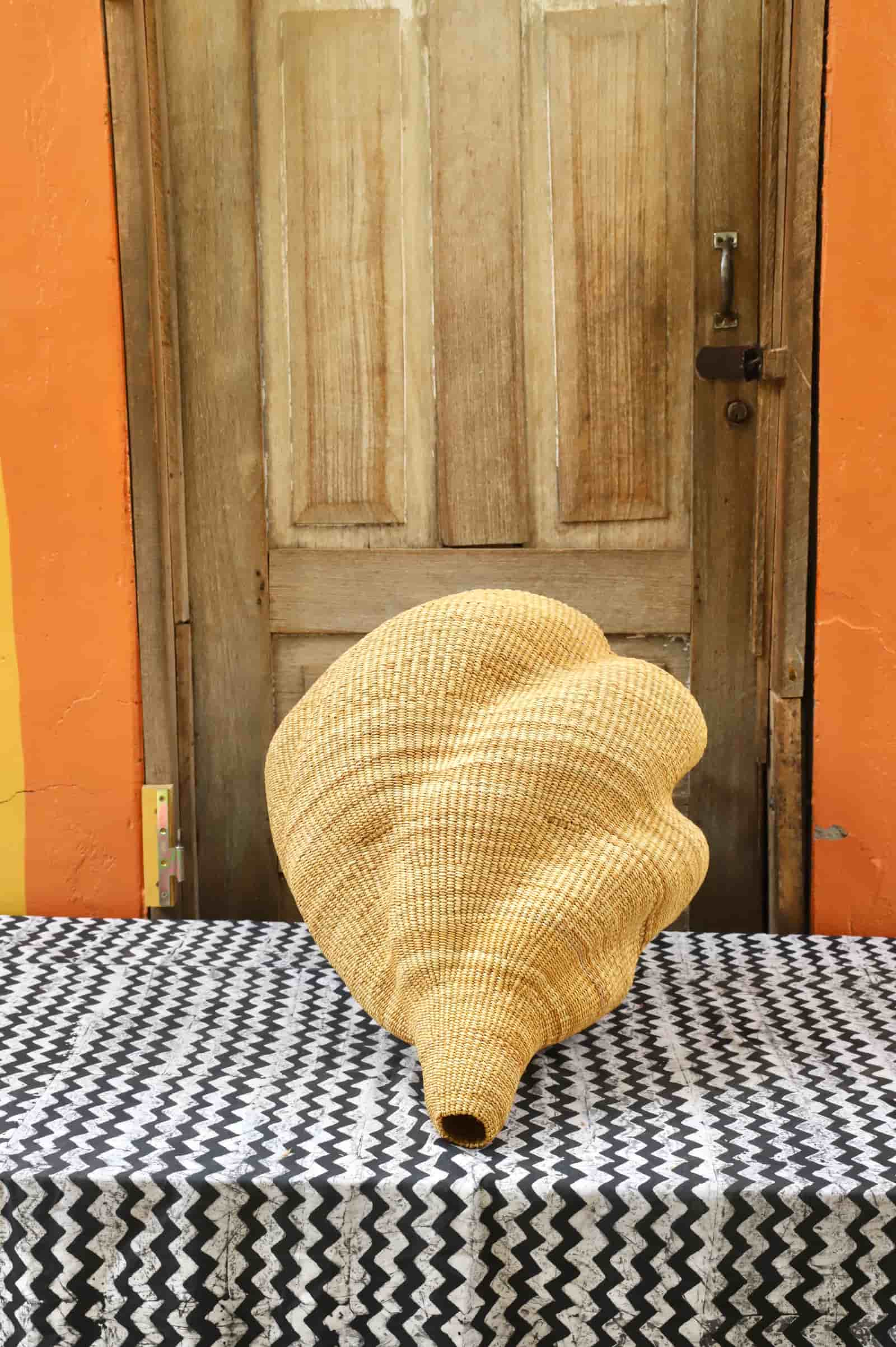 Woven conch on a black and white patterned tablecloth with an orange wall and wooden door in the background.