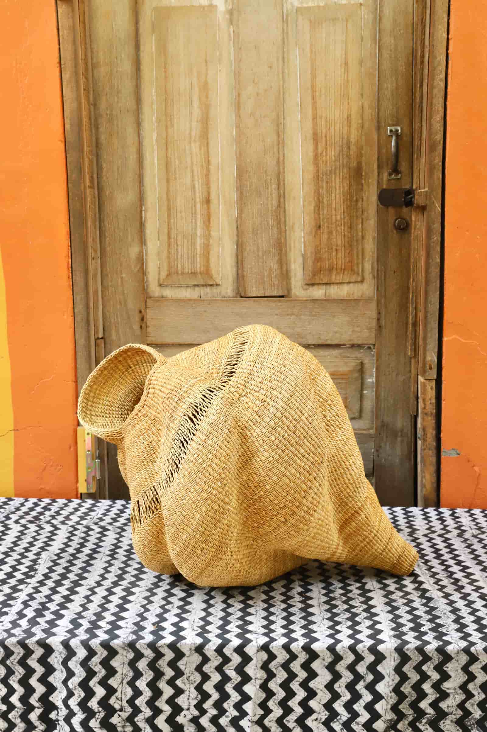 Woven conch-shaped lampshade on a black and white patterned cloth with a wooden door in the background.