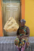 Woman in colorful dress sitting on a bench with a woven bag behind a door and yellow wall.