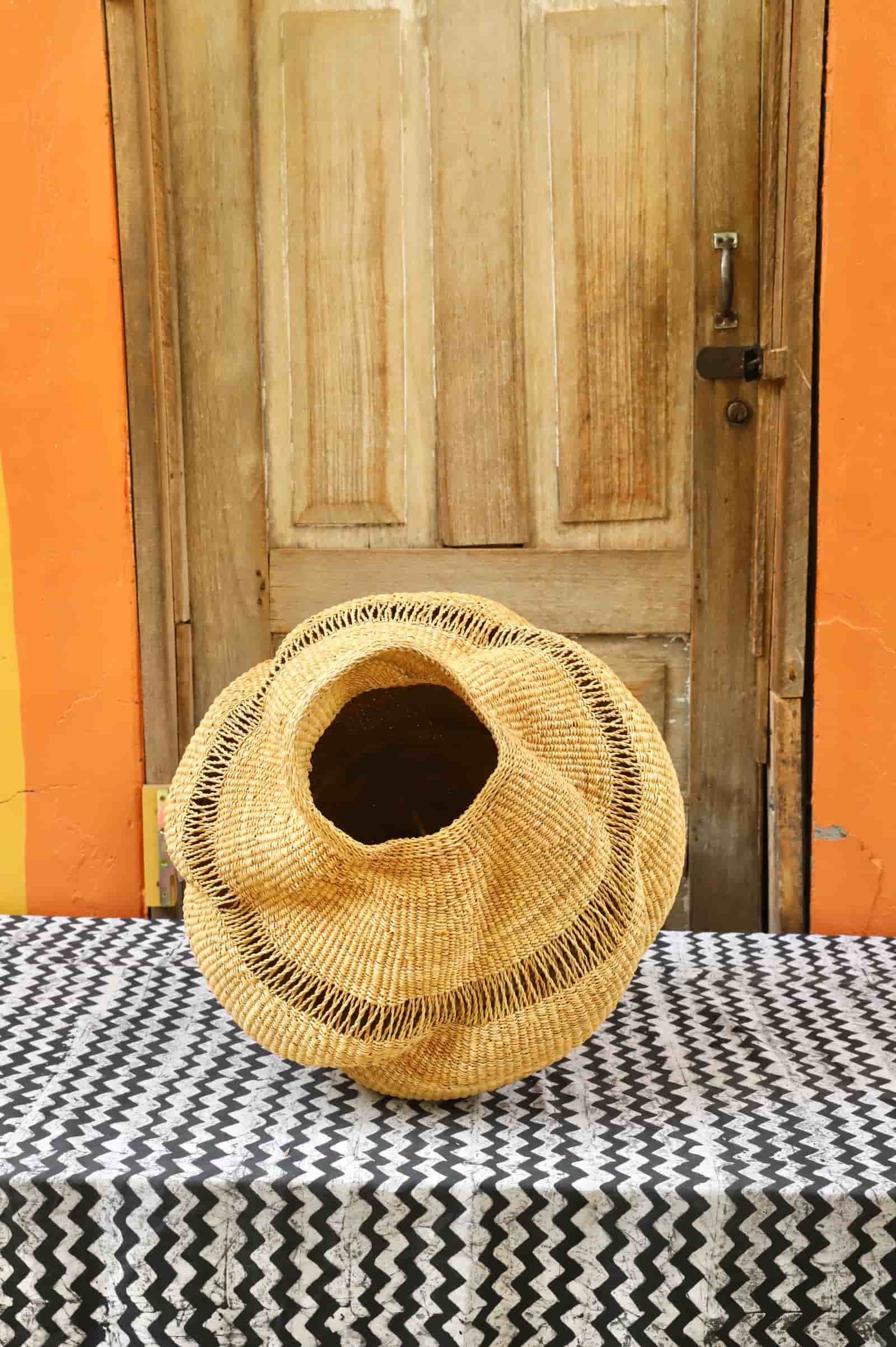 Woven conch-shaped lampshade on a black and white patterned cloth with a wooden door in the background.