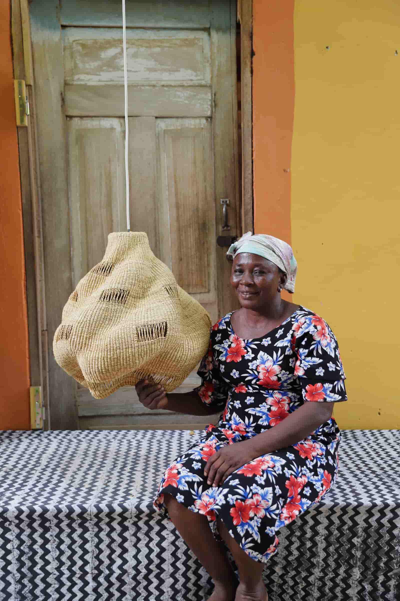 Woman holding a woven basket in front of a yellow wall and wooden door.