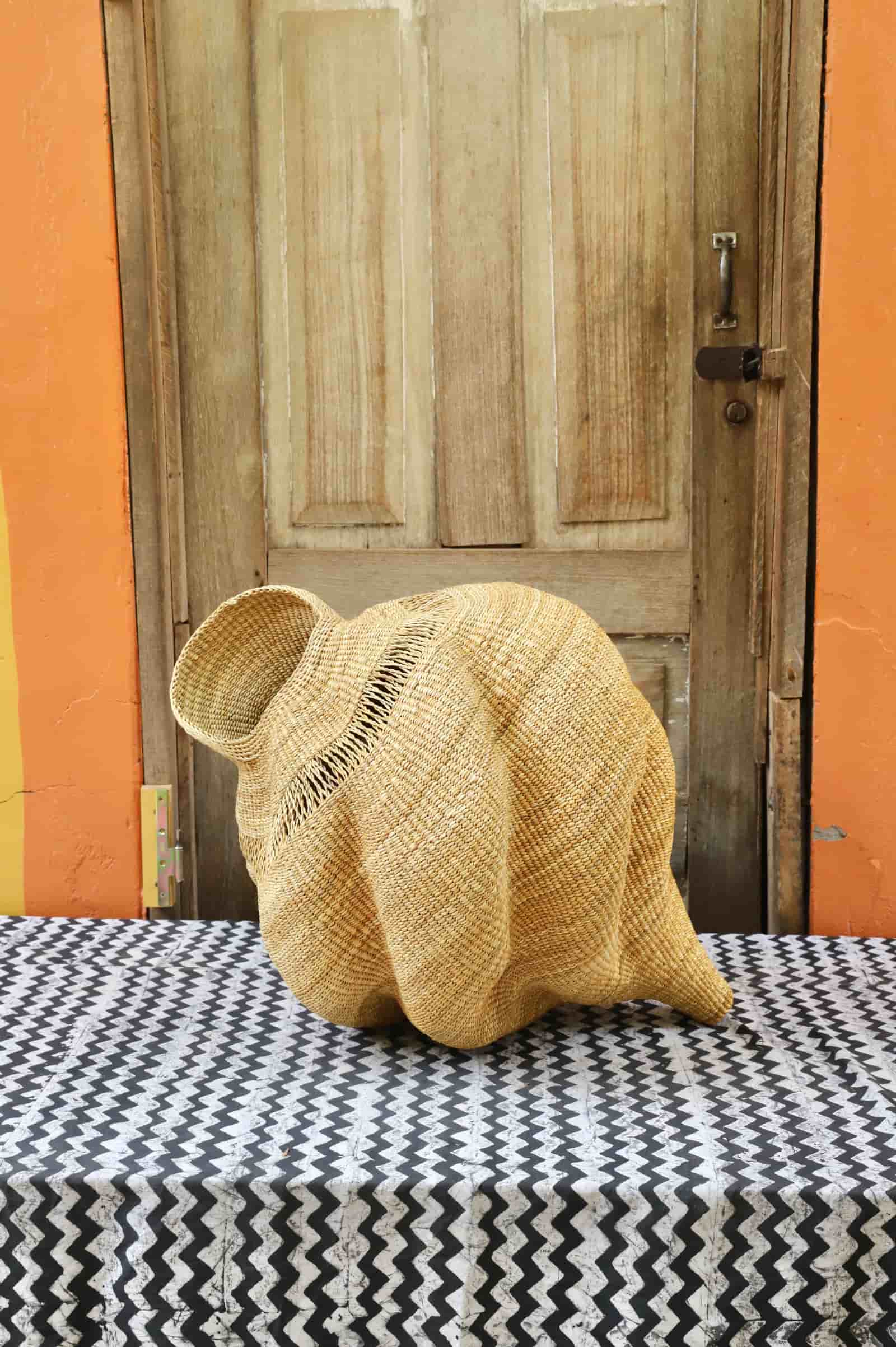 Woven conch-shaped lampshade on a black and white patterned cloth with a wooden door in the background.