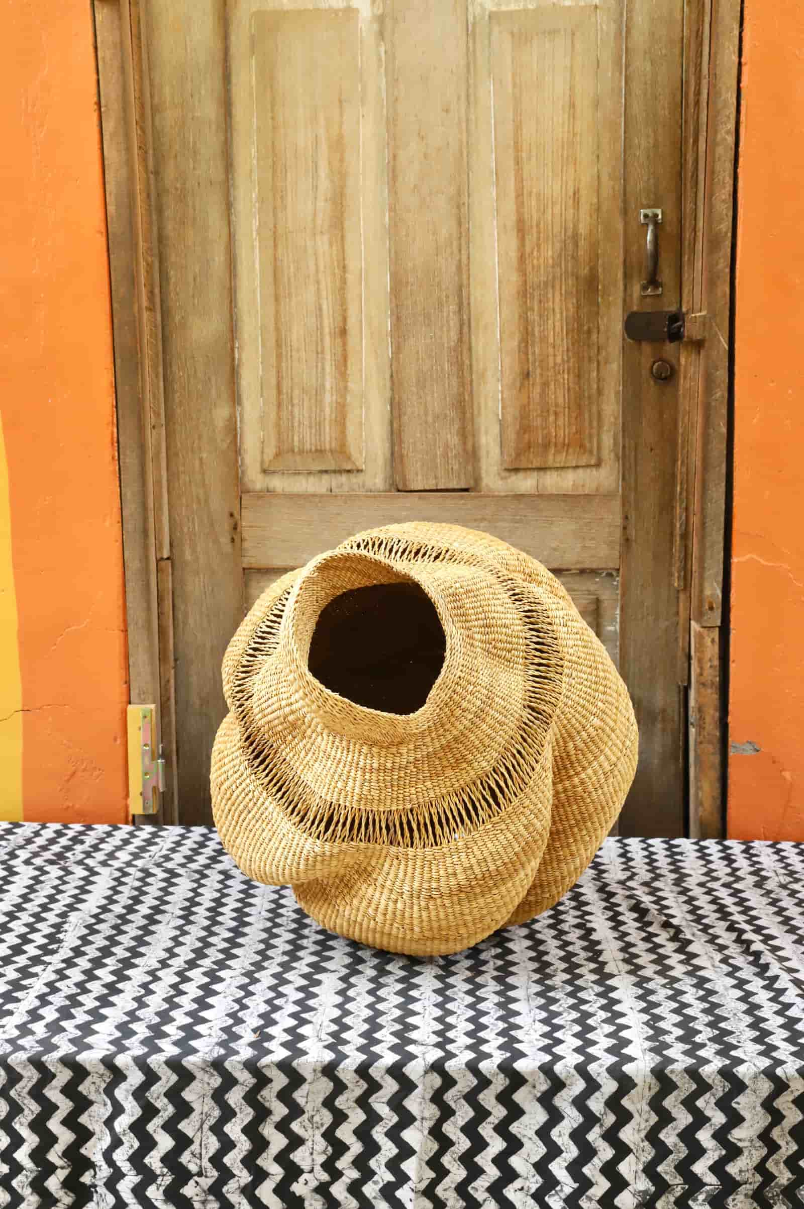 Woven conch-shaped lampshade on a black and white patterned cloth with a wooden door in the background.