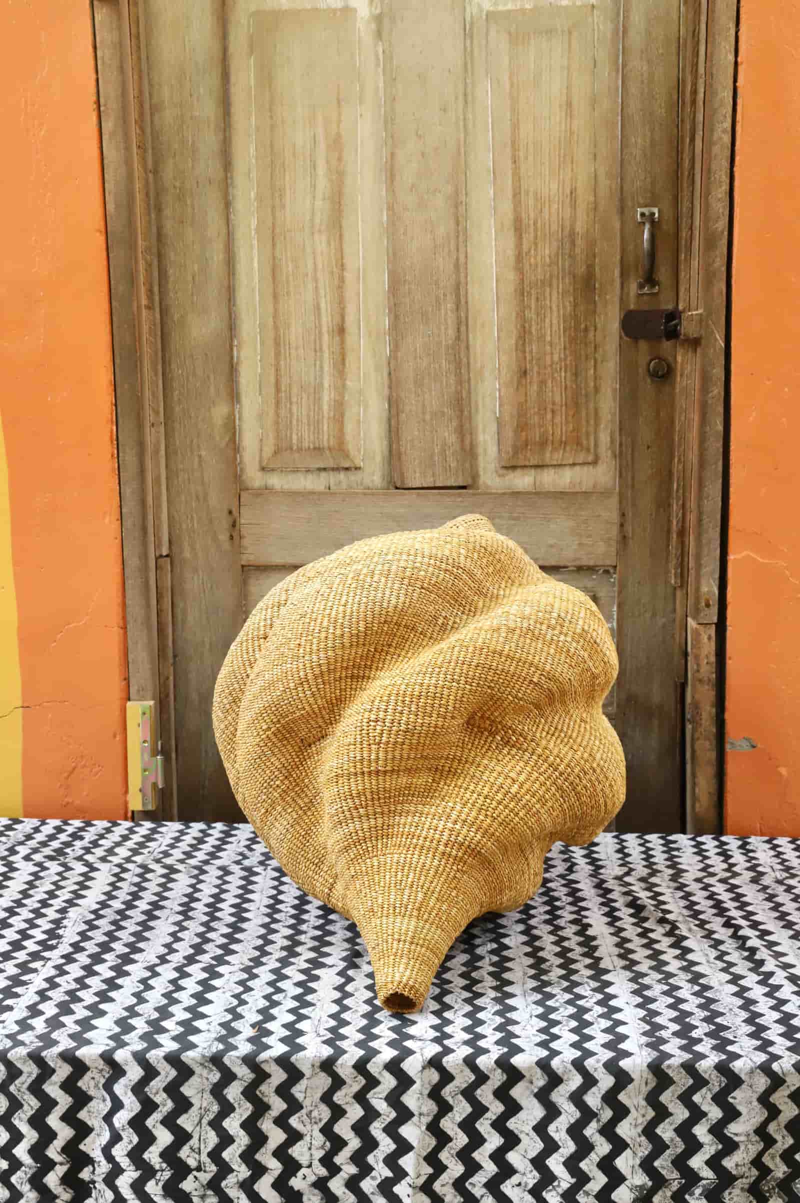 Woven conch-shaped lampshade on a black and white patterned cloth with a wooden door in the background.
