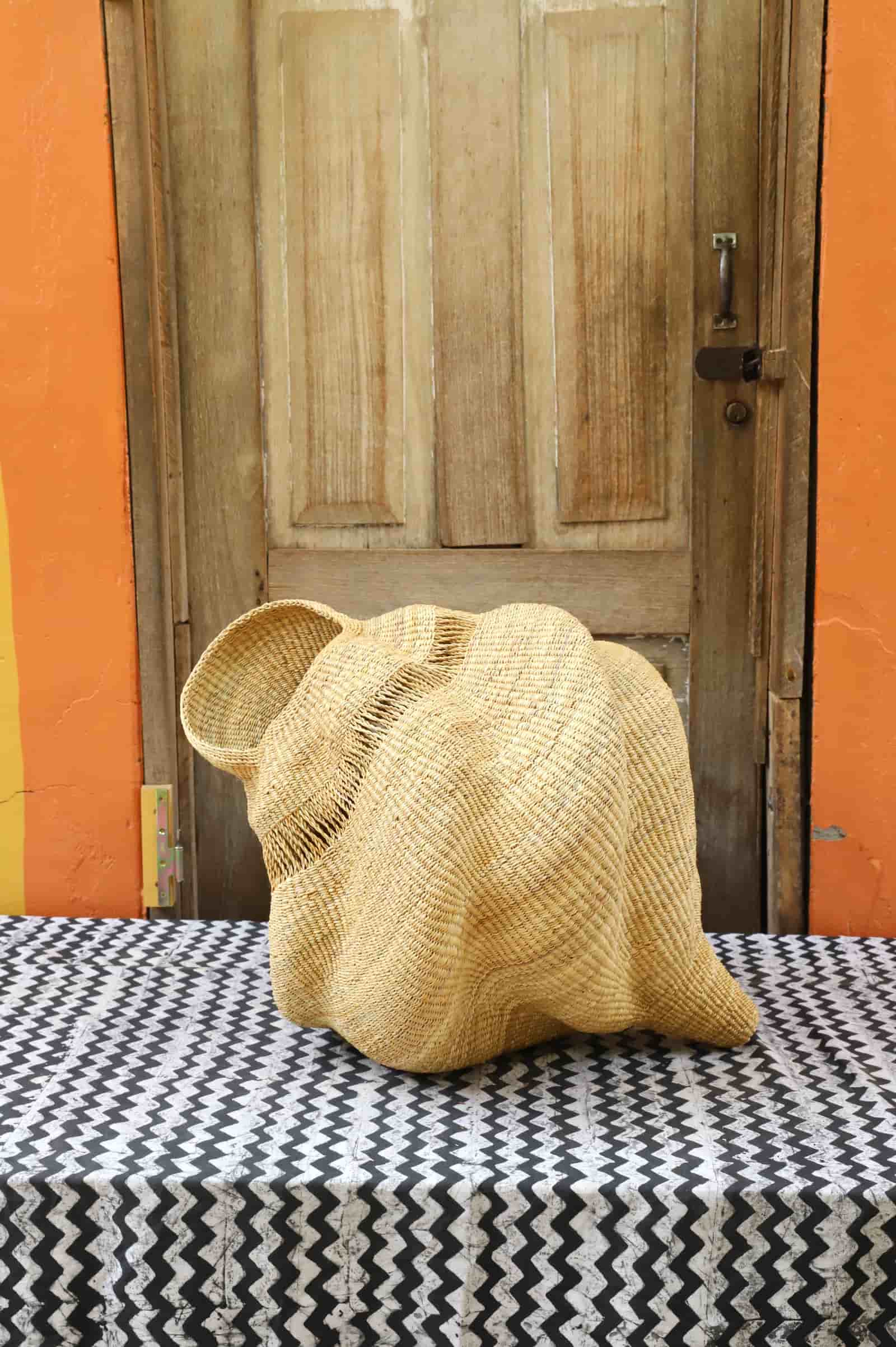 Woven conch-shaped lampshade on a black and white patterned cloth with a wooden door in the background.