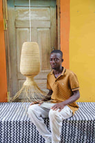 Man sitting on a bed with a woven lamp in a room with orange walls and a wooden door.