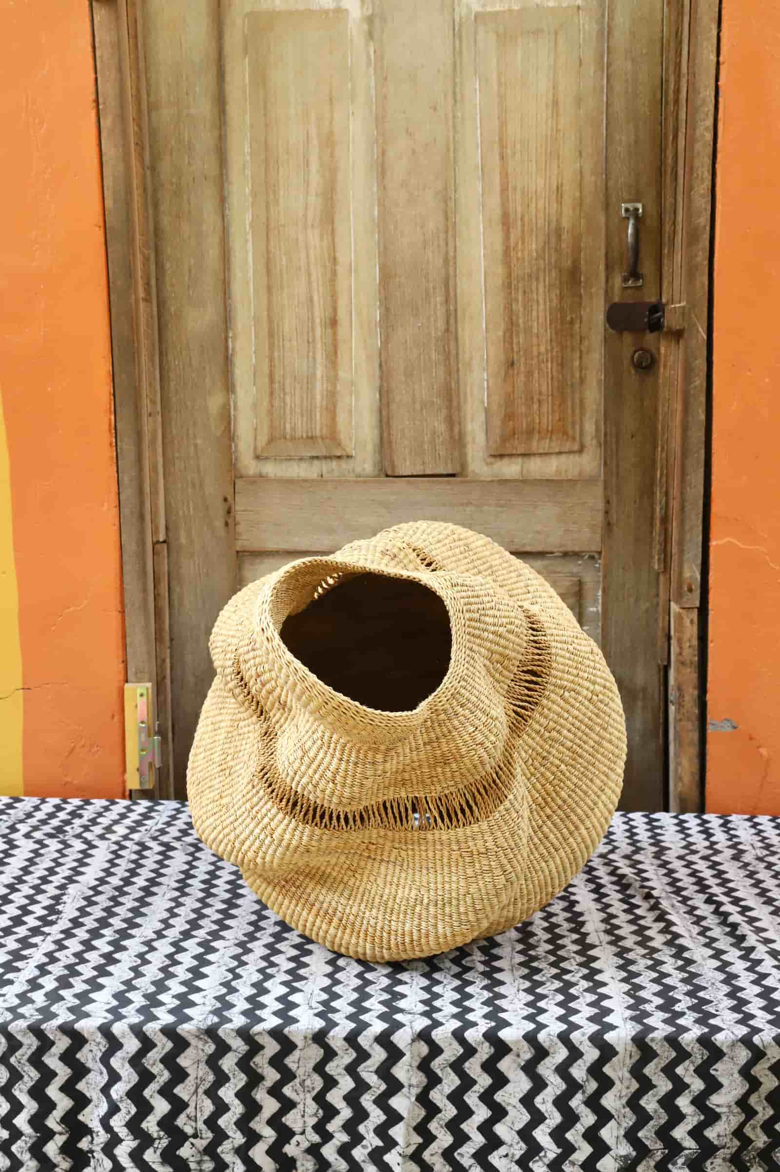 Woven conch-shaped lampshade on a black and white patterned cloth with a wooden door in the background.