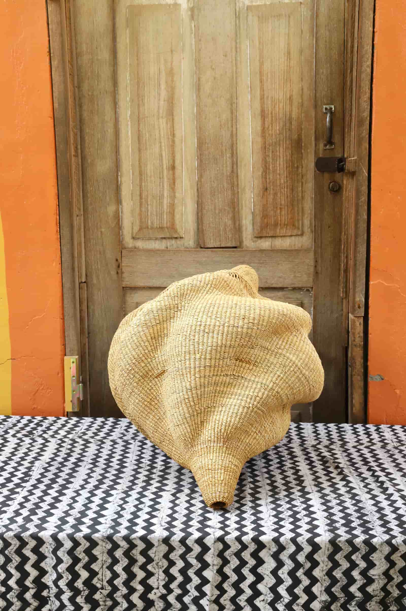 Woven conch-shaped lampshade on a black and white patterned cloth with a wooden door in the background.