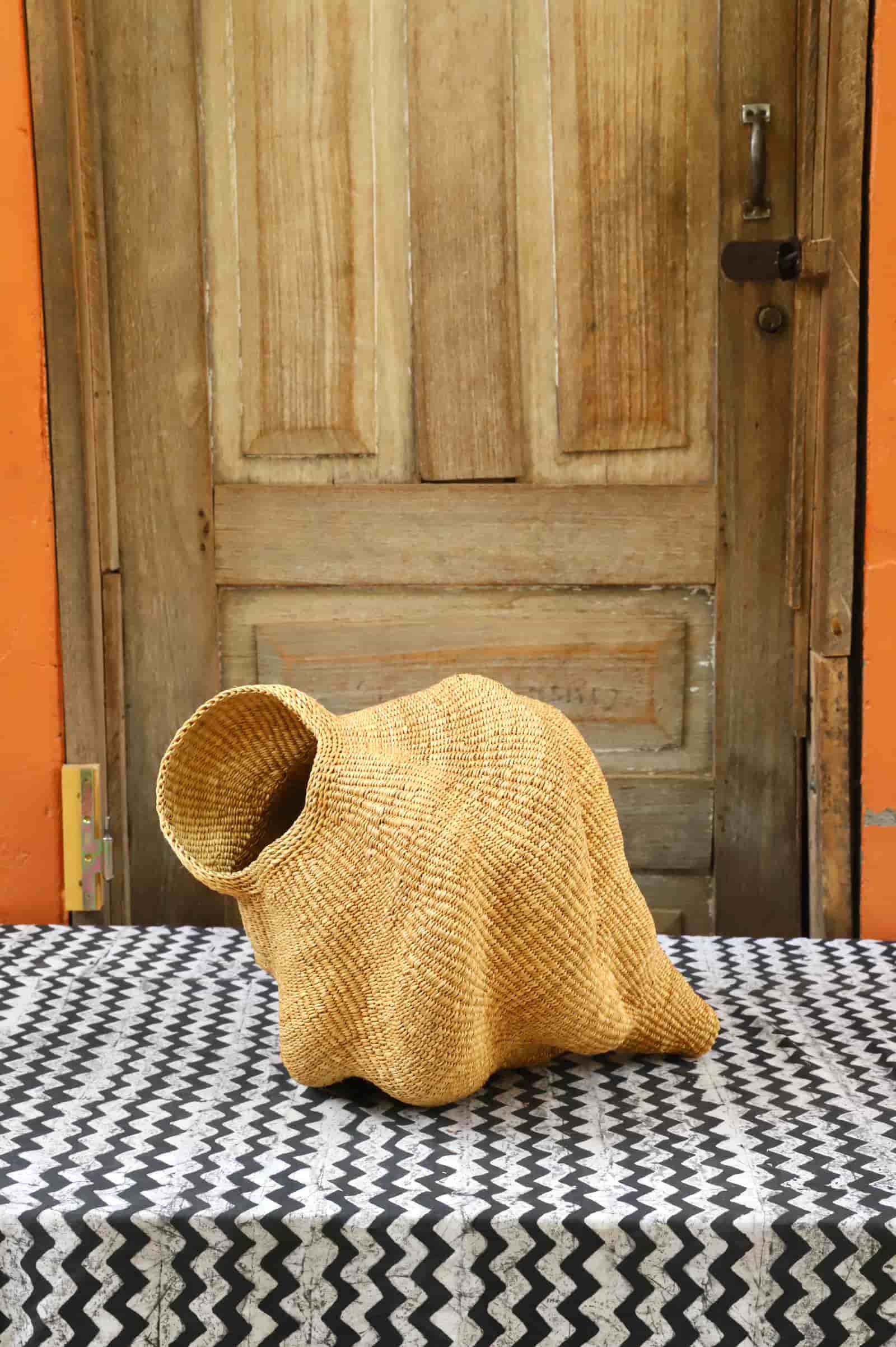 Woven conch-shaped lampshade on a black and white patterned cloth with a wooden door in the background.