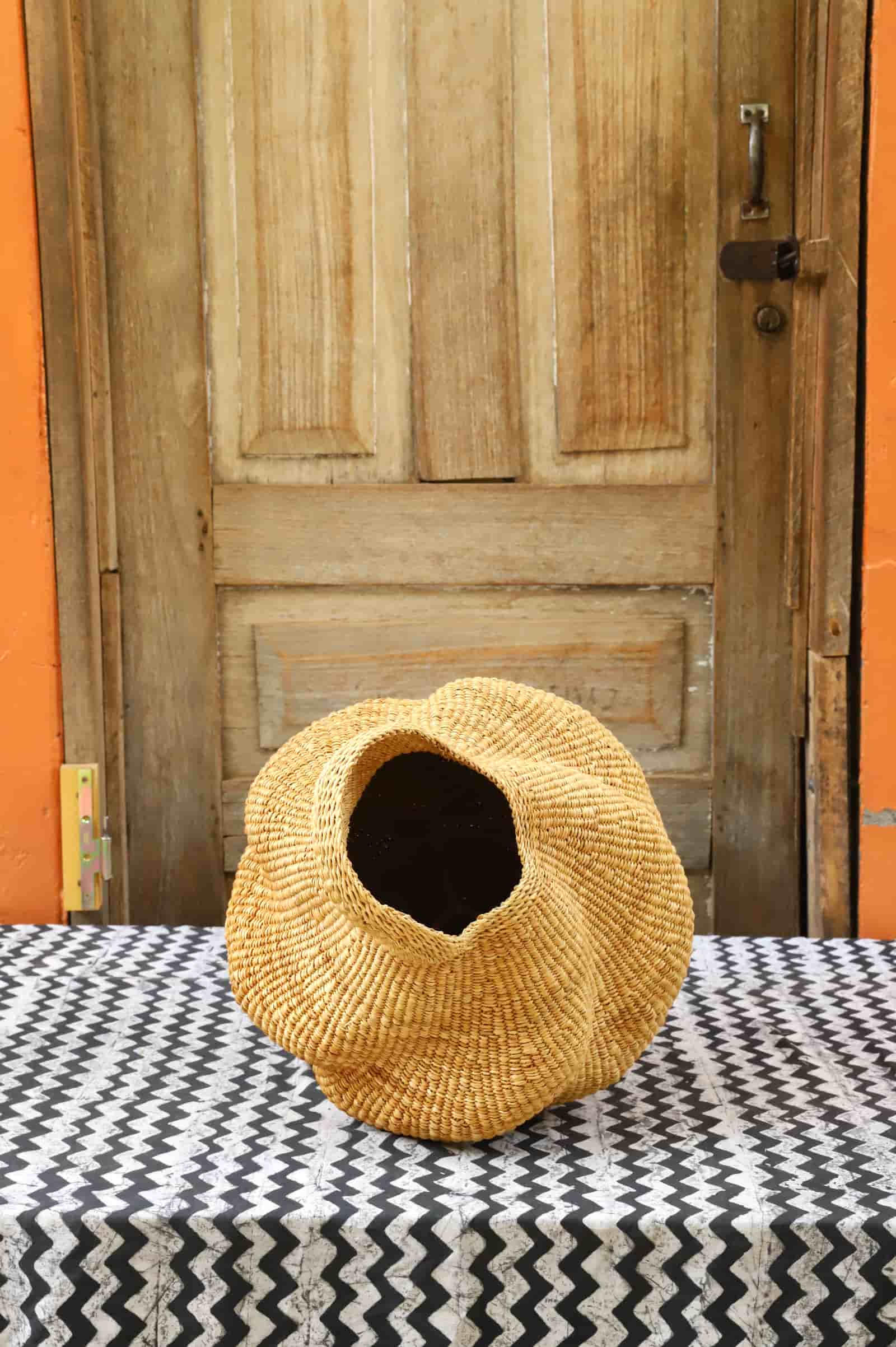 Woven conch-shaped lampshade on a black and white patterned cloth with a wooden door in the background.