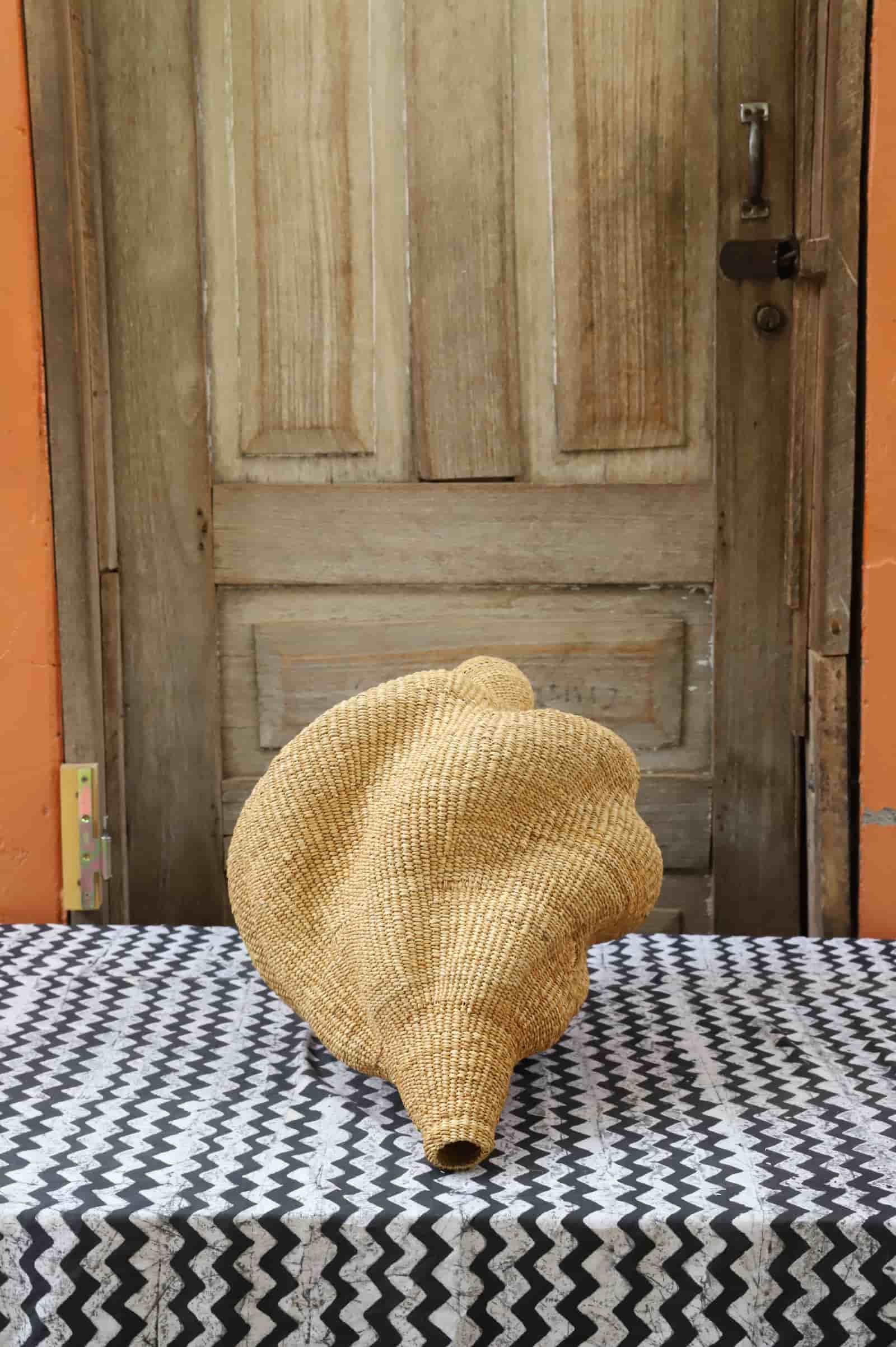 Woven conch-shaped lampshade on a black and white patterned cloth with a wooden door in the background.