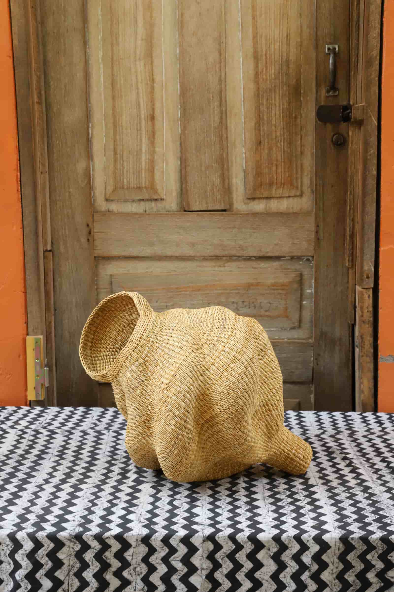 Woven conch-shaped lampshade on a black and white patterned cloth with a wooden door in the background.