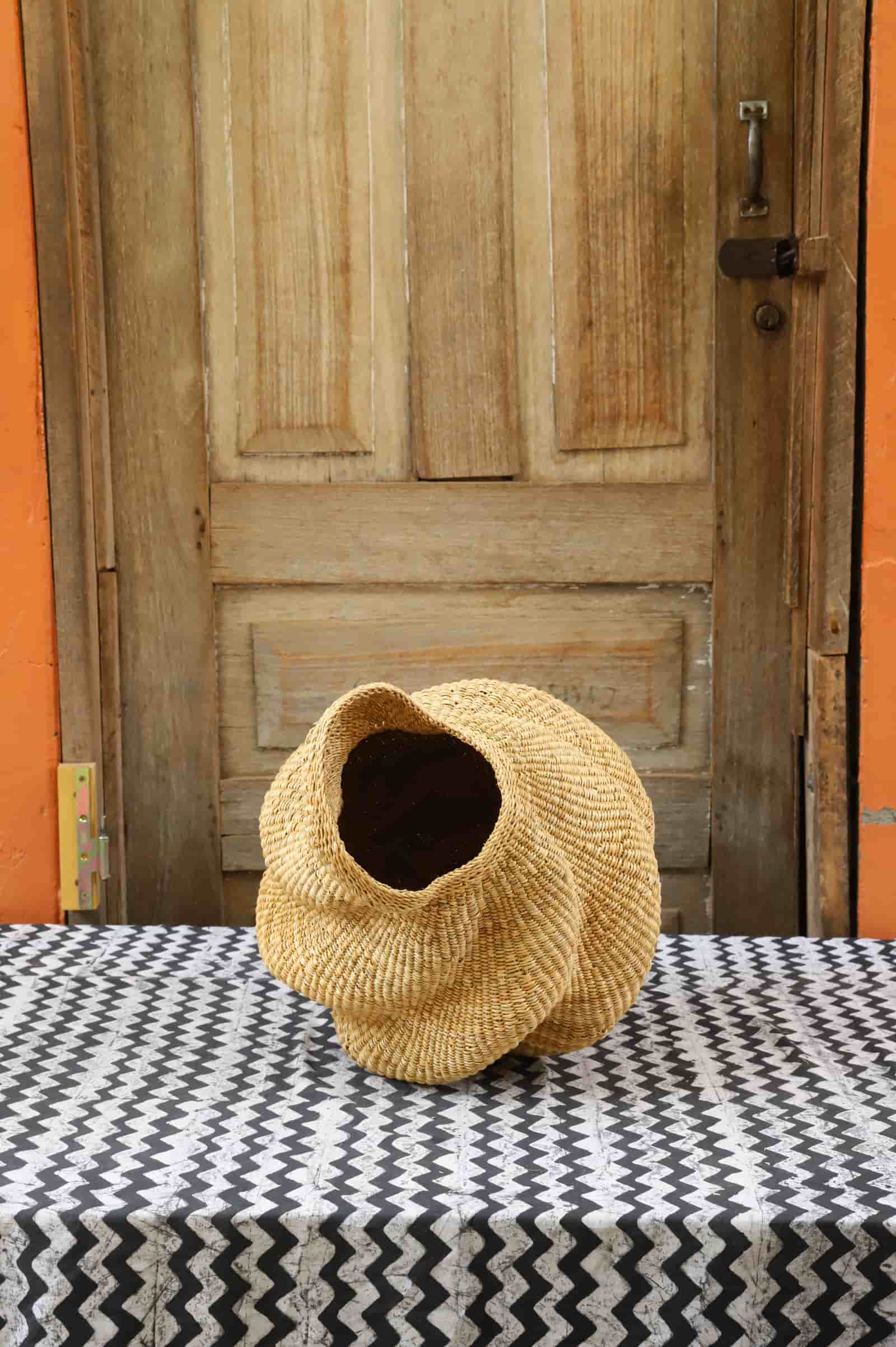 Woven conch-shaped lampshade on a black and white patterned cloth with a wooden door in the background.