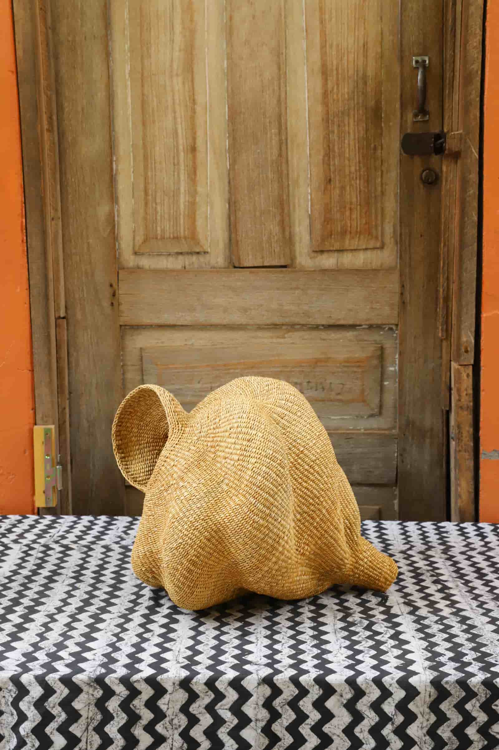 Woven conch lampshade on a black and white patterned tablecloth with a wooden door in the background.