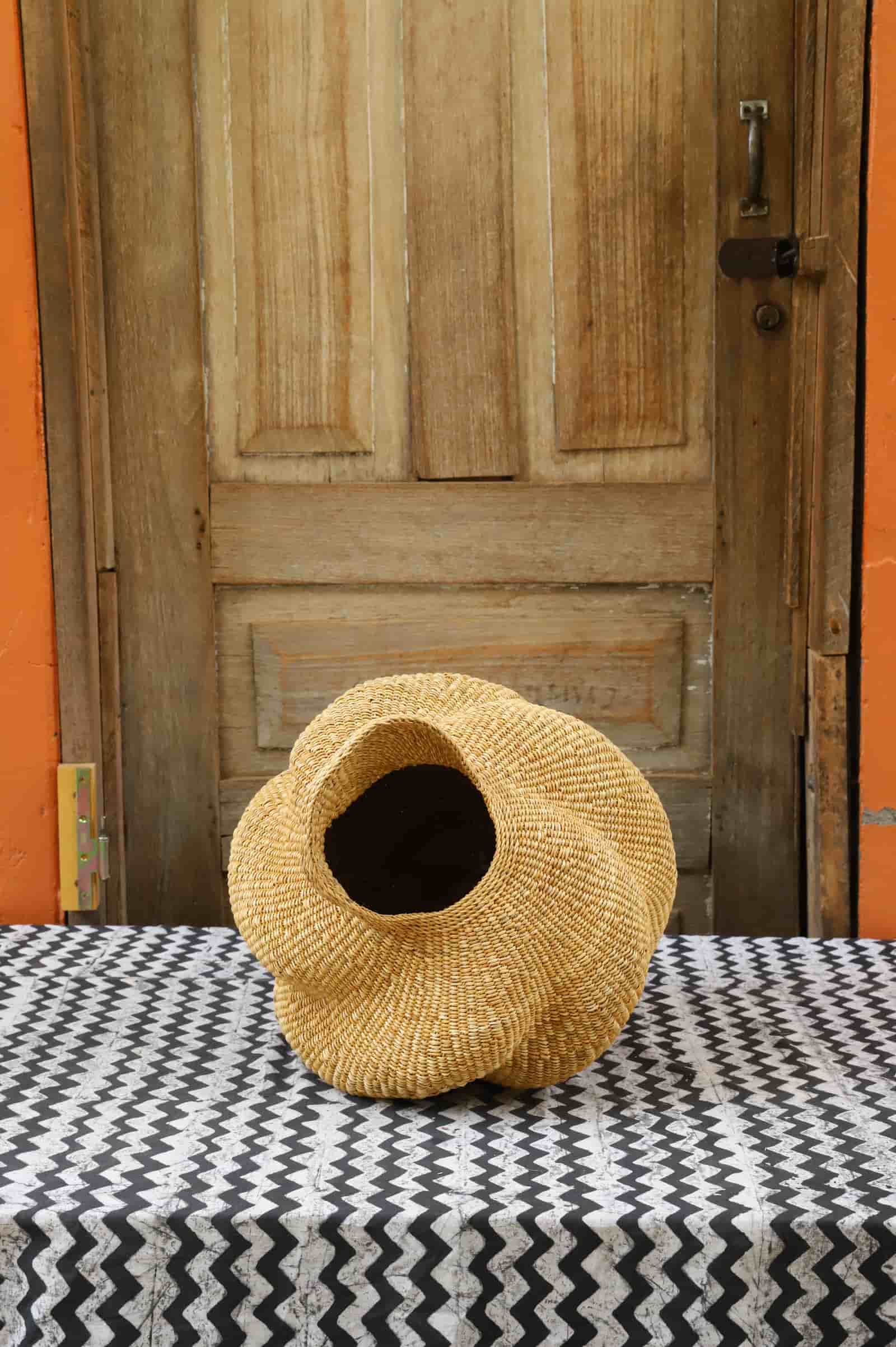 Woven conch lampshade on a black and white patterned tablecloth with a wooden door in the background.