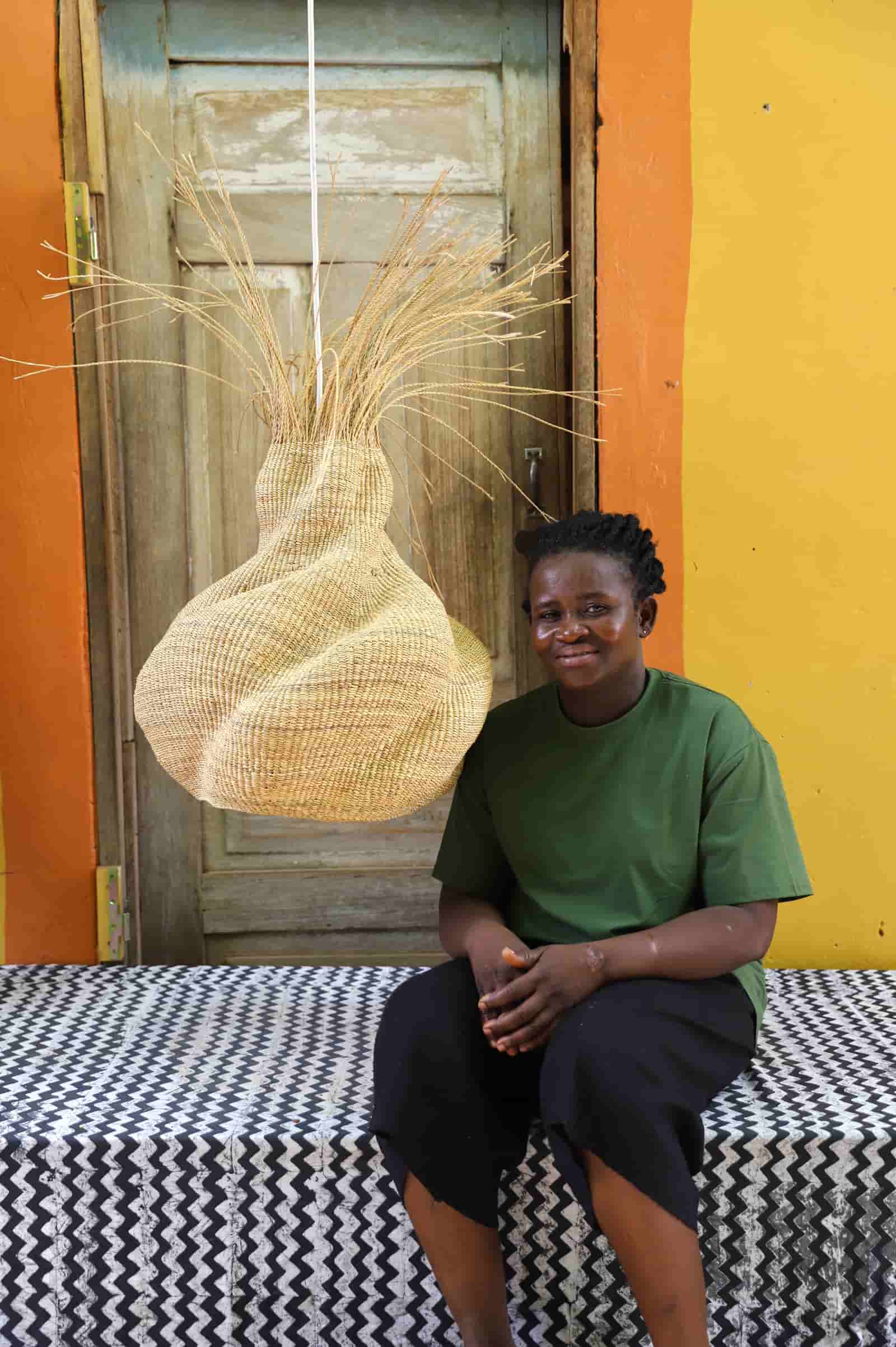 Person sitting on a bench with a large woven basket in front of a colorful wall.