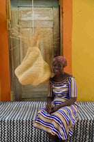 Woman sitting on a bed with a woven basket against a colorful wall.