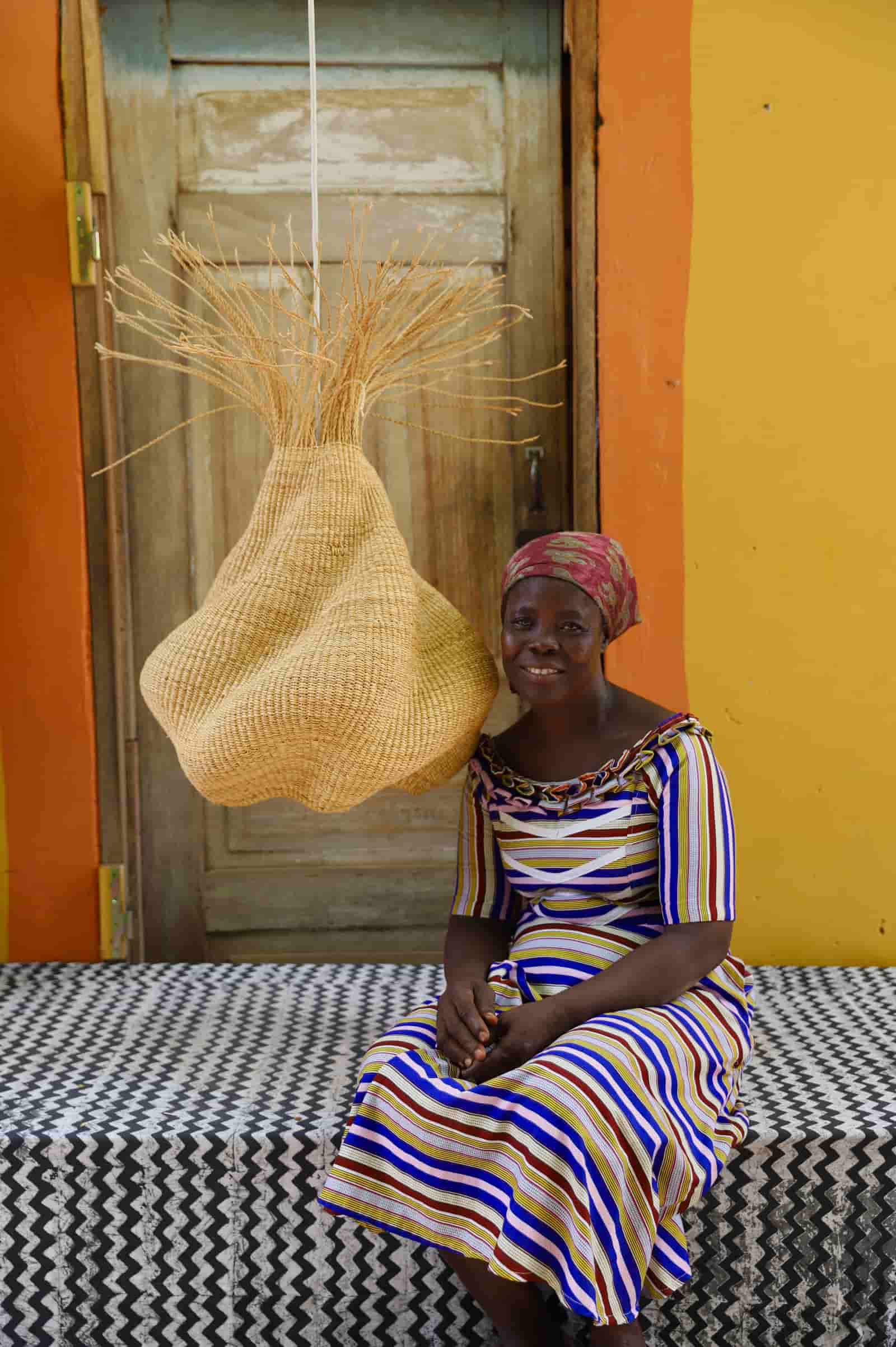 Woman sitting on a bed with a woven basket against a colorful wall.