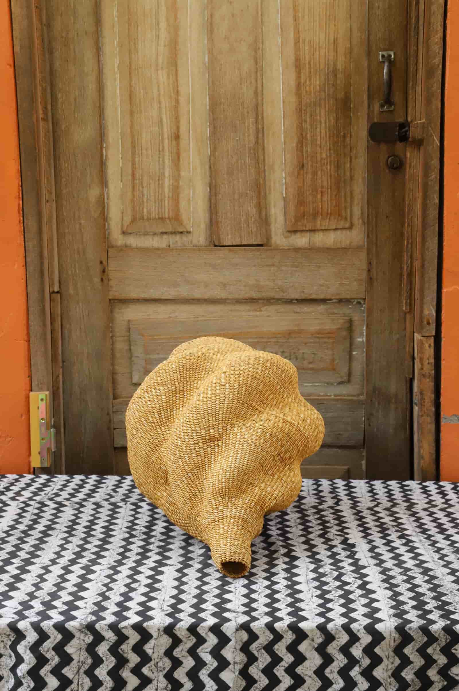 Woven conch lampshade on a black and white patterned tablecloth with a wooden door in the background.