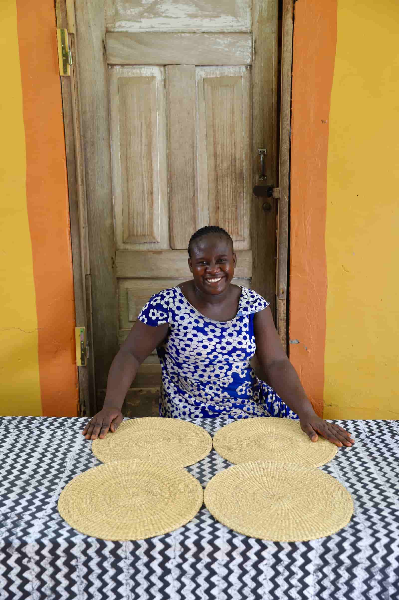 Artisan sitting with woven placemats on a black and white cloth against a wooden door.