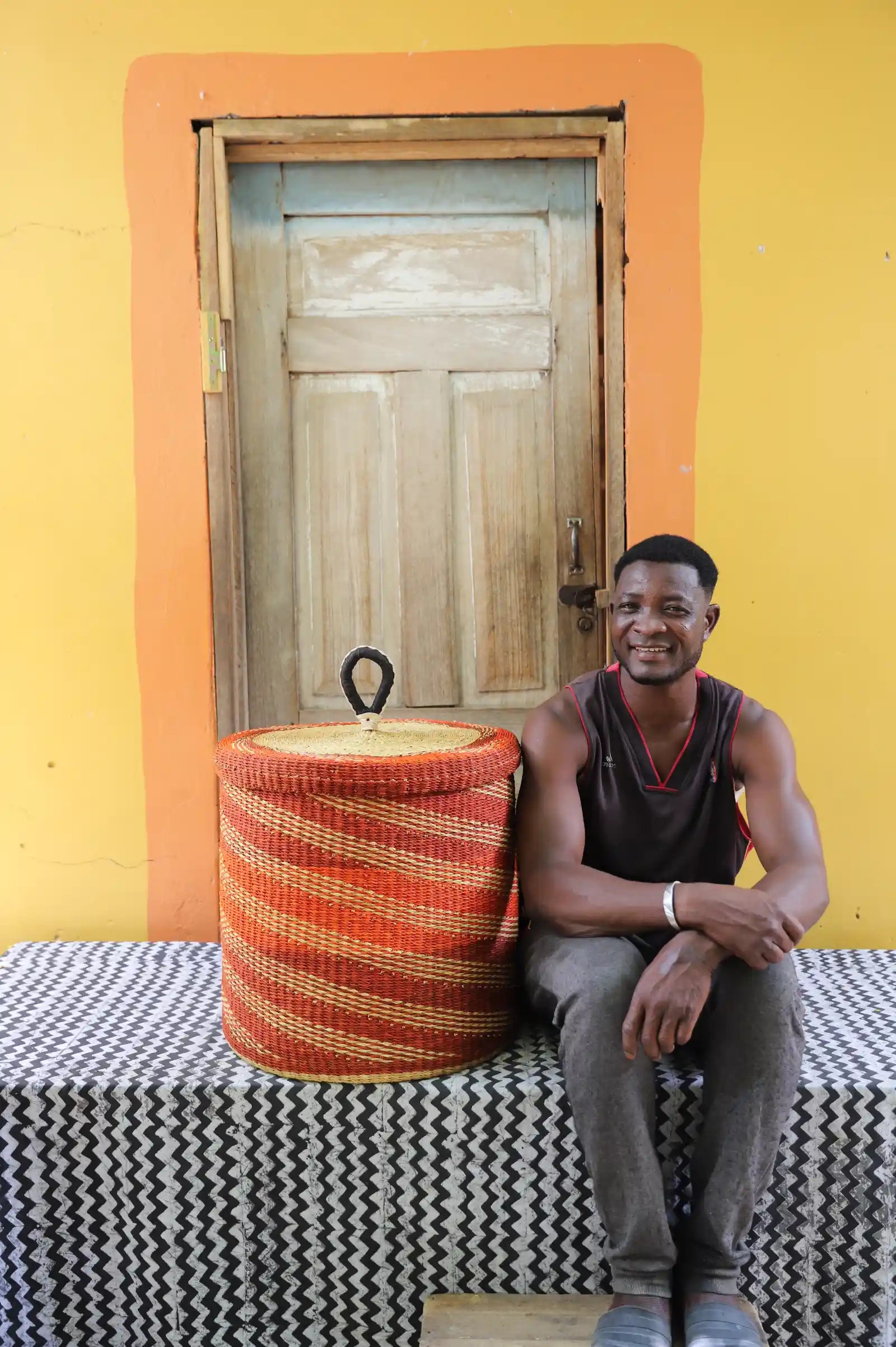 Handwoven Bolga laundry basket dyed rust-orange, beside a seated man in a dark vest.