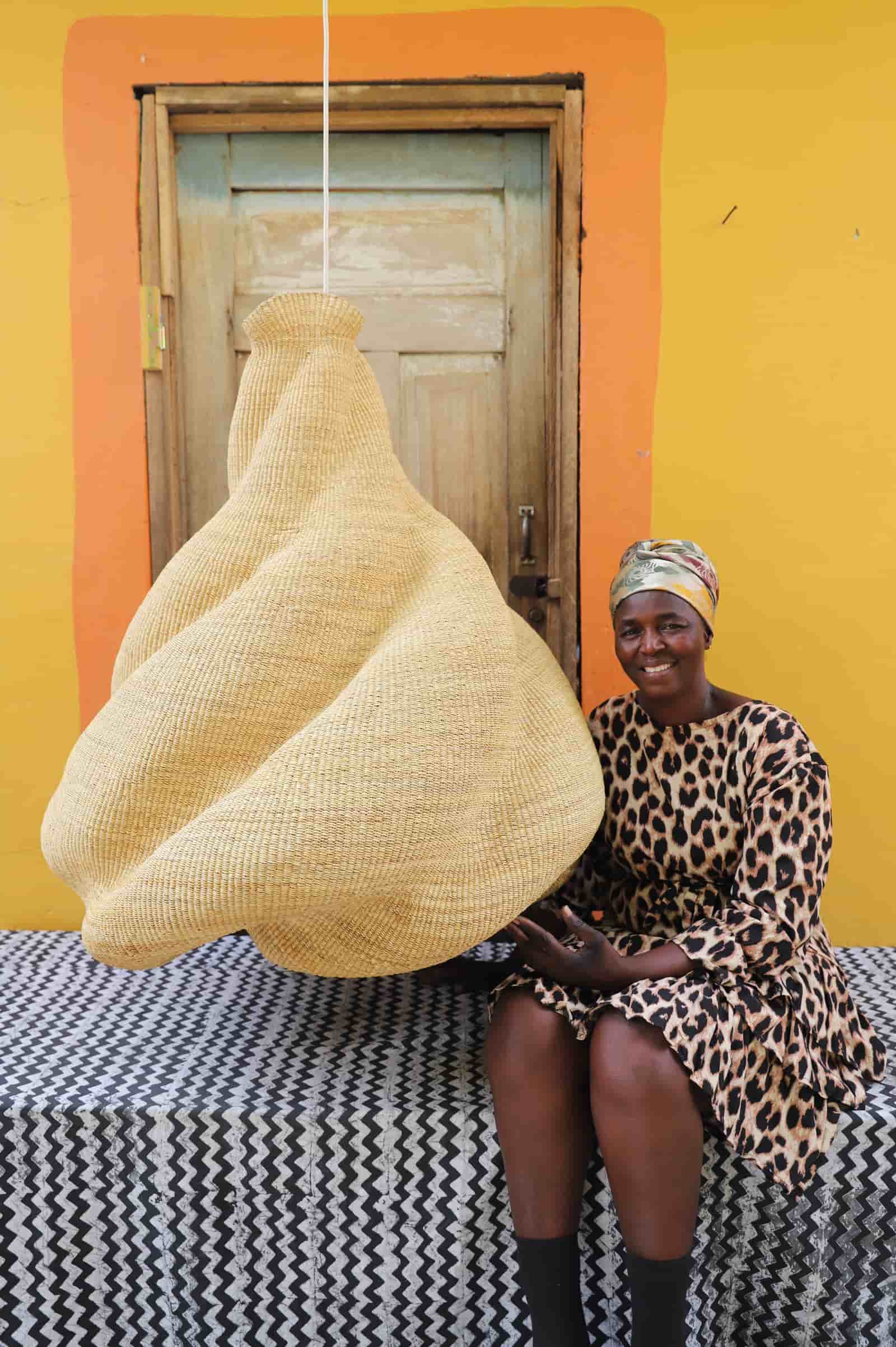 Woman sitting next to a large woven basket against a yellow wall.