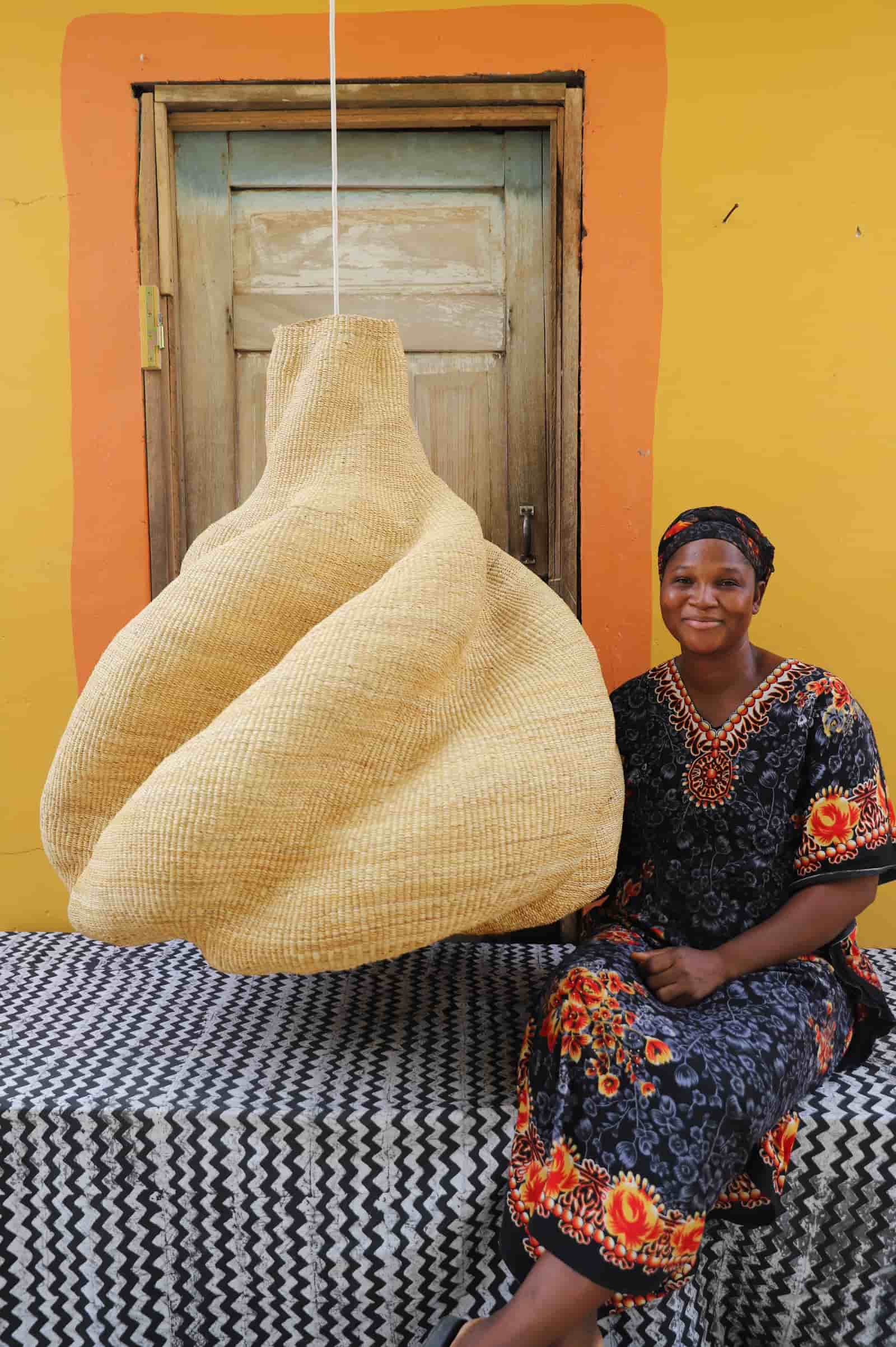 Woman sitting next to a large woven basket against a yellow wall.
