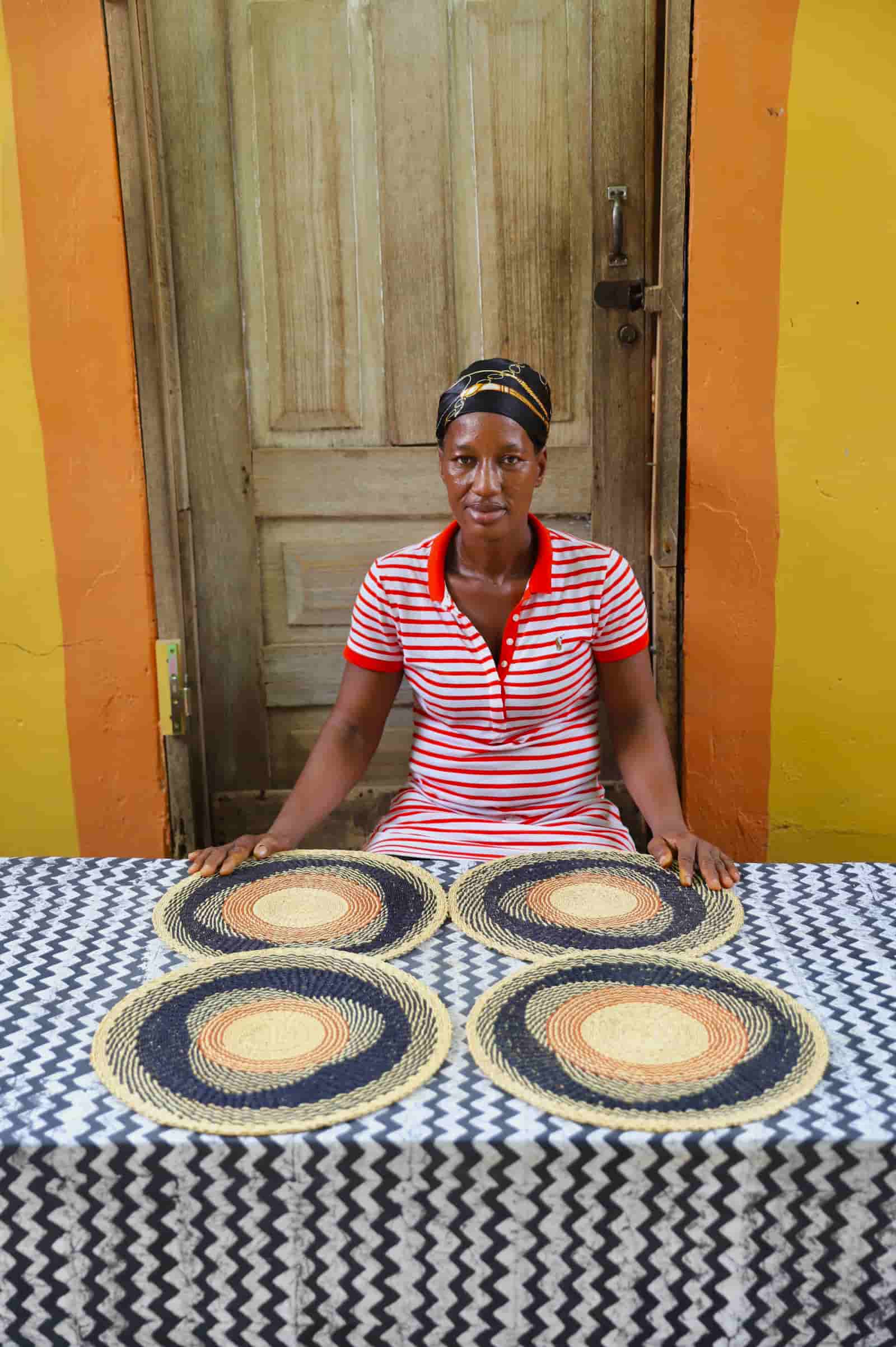 Artisan sitting with woven placemats on a black and white cloth against a wooden door.