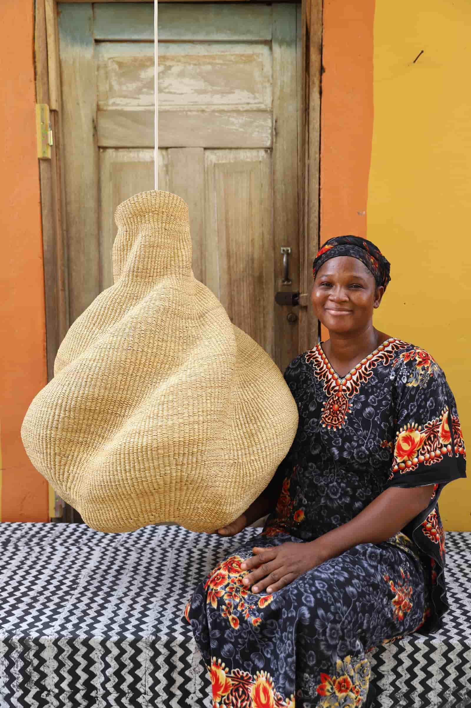 Woman sitting on a bed with a large woven basket in front of a wooden door.