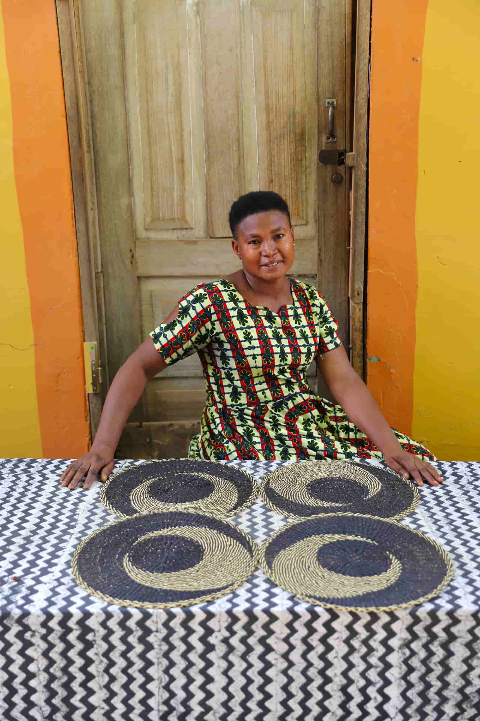 Artisan sitting with woven placemats on a black and white cloth against a wooden door.