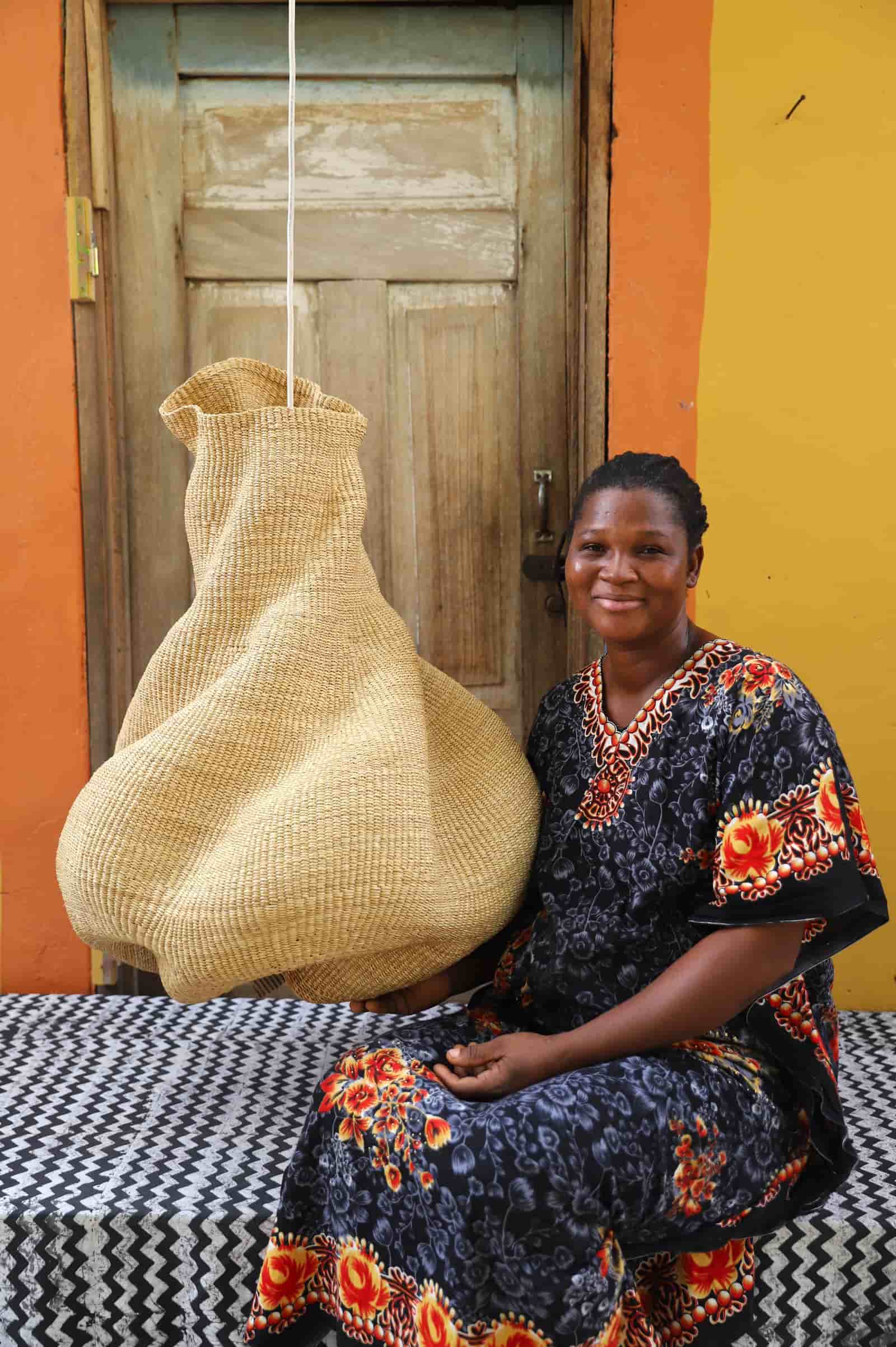 Woman sitting on a bench with a woven basket against an orange wall.