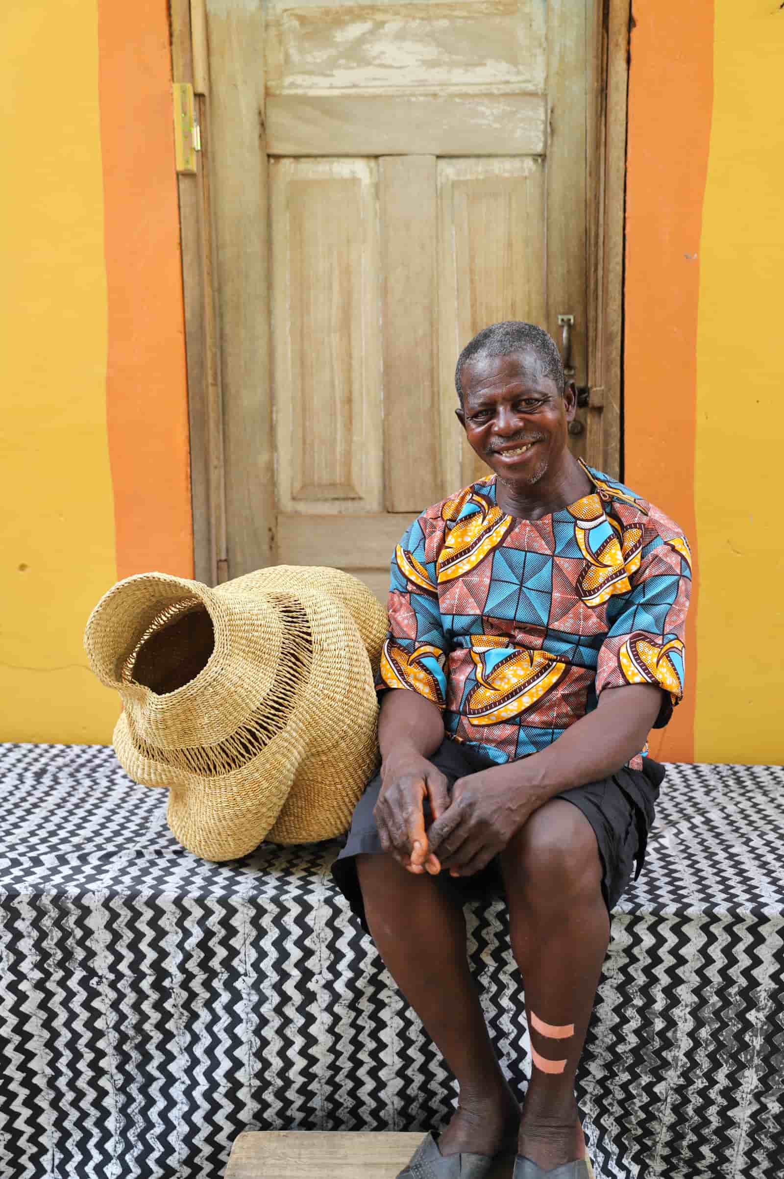 Man sitting on a bench with a woven conch lampshade against a colorful wall.
