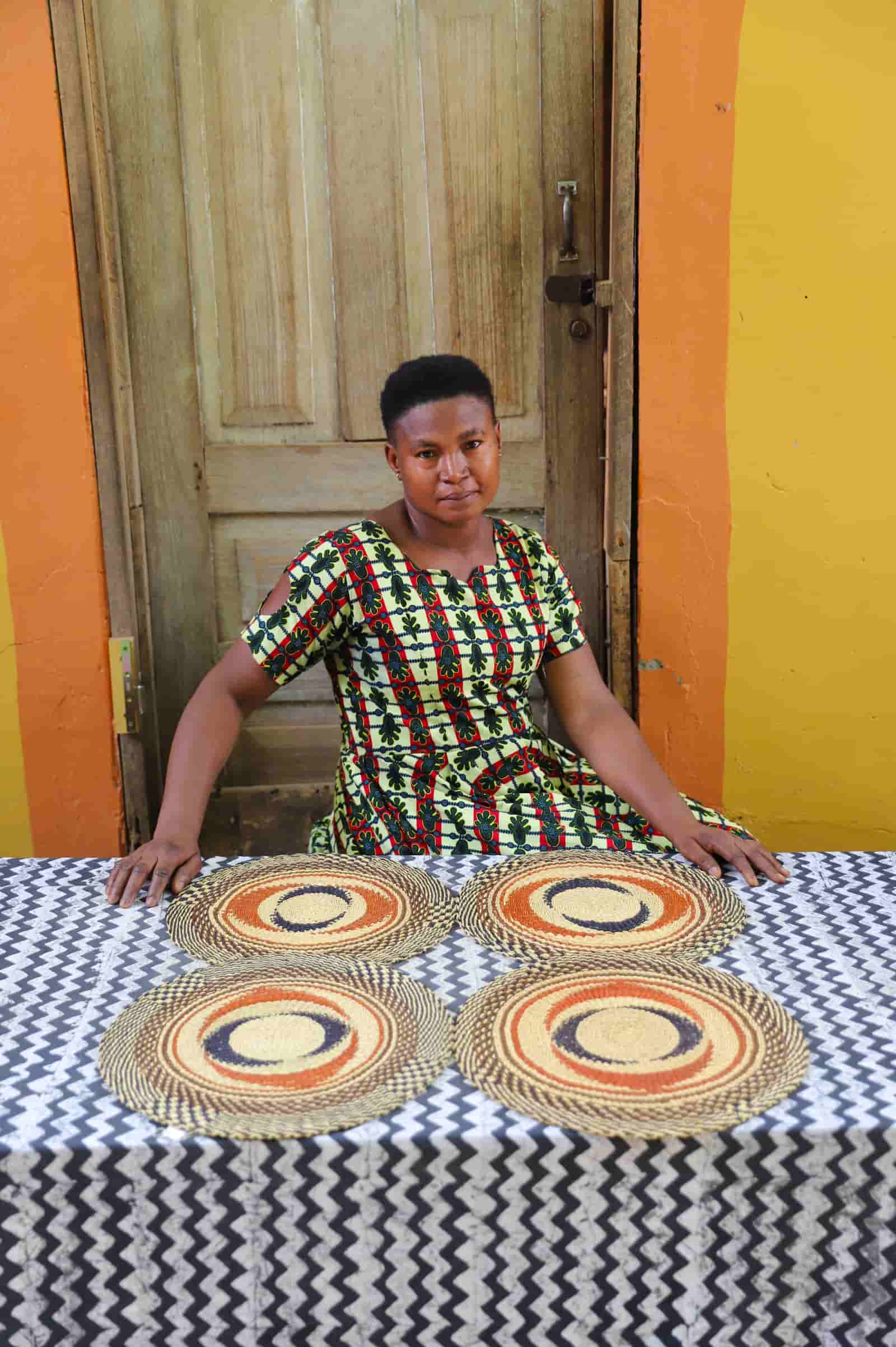 Artisan sitting with woven placemats on a black and white cloth against a wooden door.
