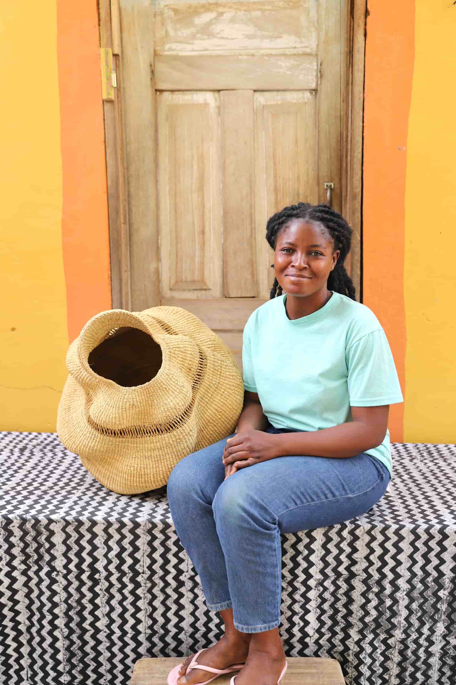 Woman sitting on a bench with a woven conch-shaped lampshade on a black and white cloth against a wooden door.