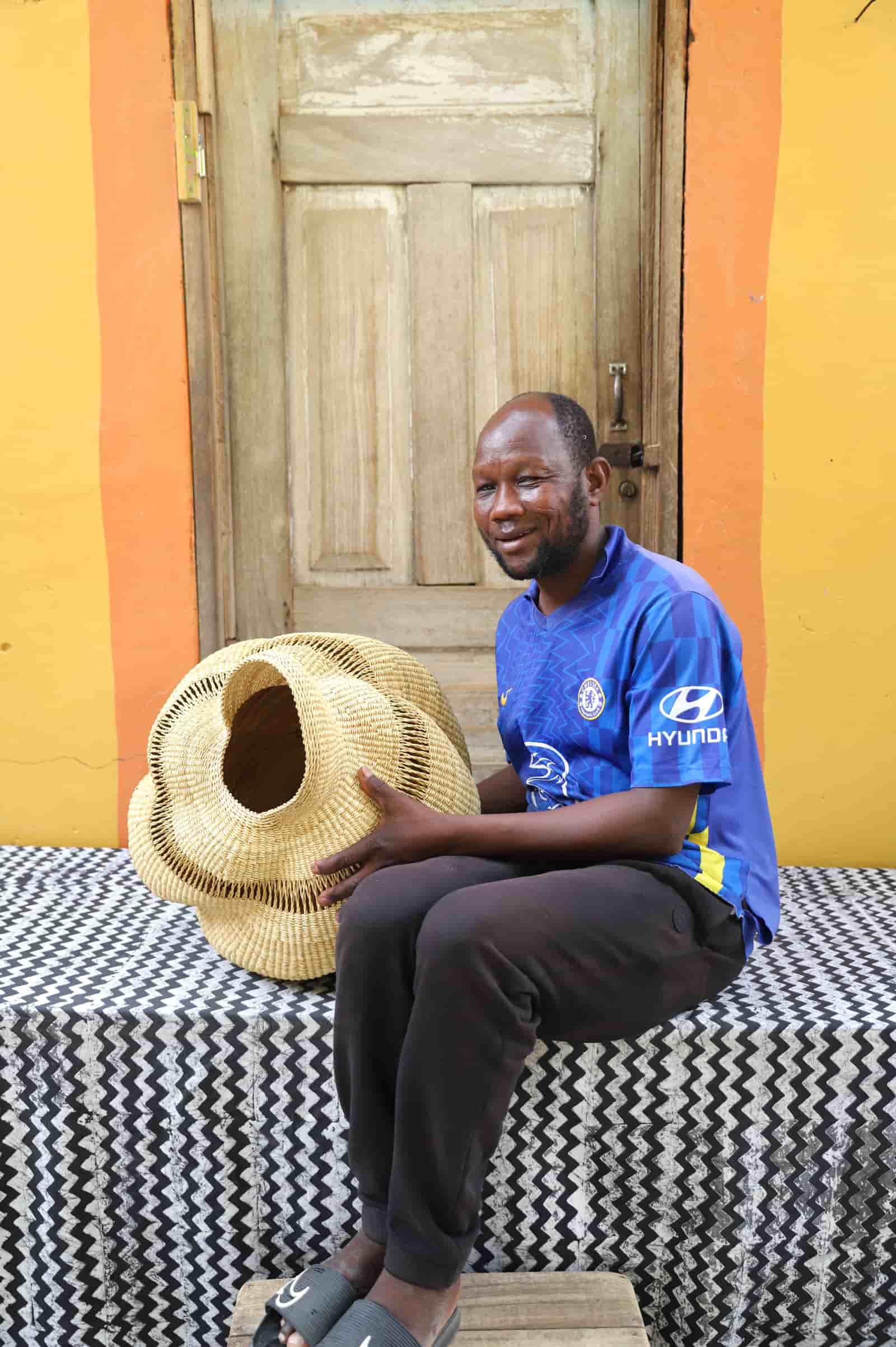 Man sitting with a conch-shaped lampshade on a black and white cloth against a wooden door.