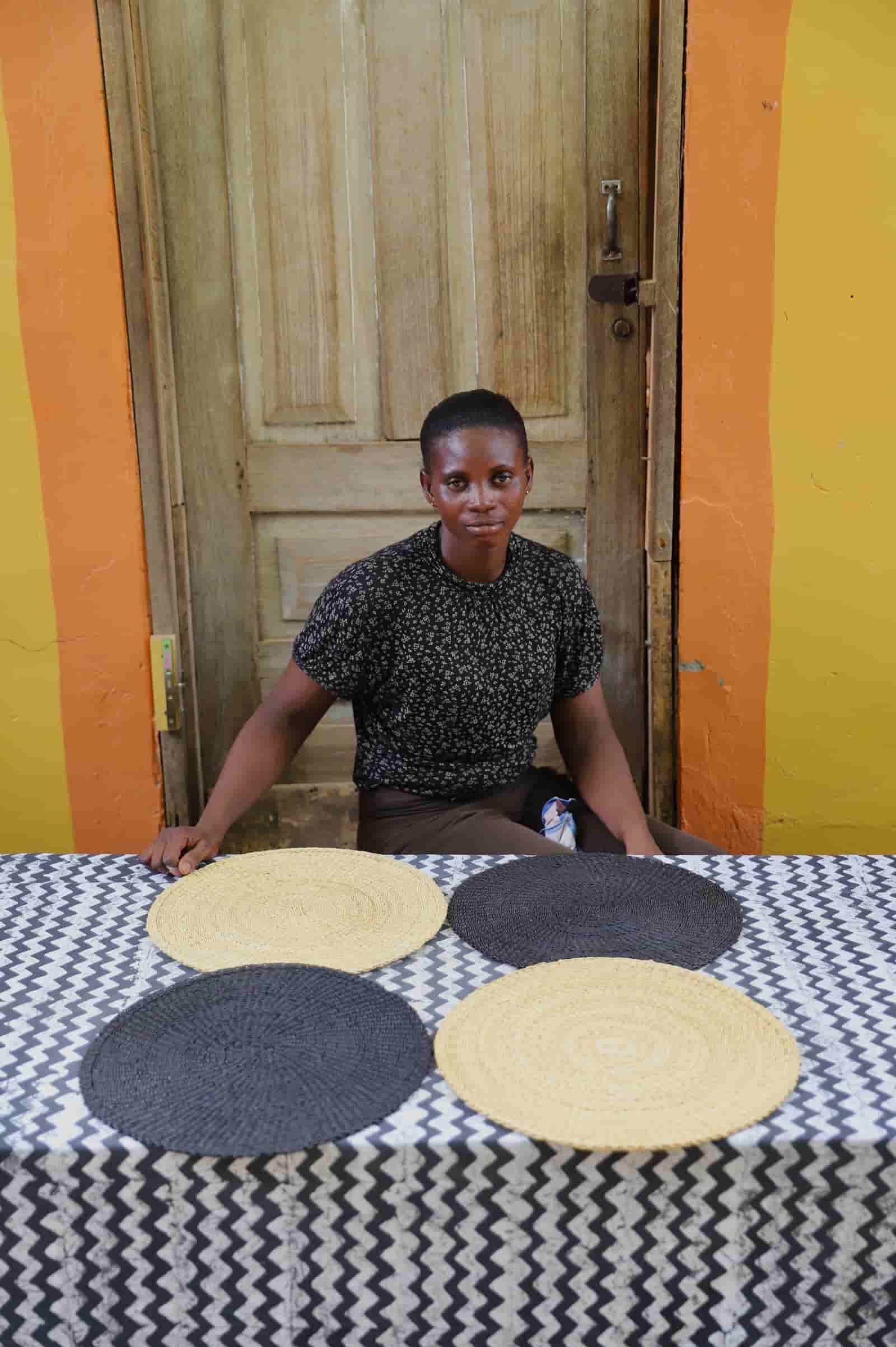 Artisan sitting with woven placemats on a black and white cloth against a wooden door.