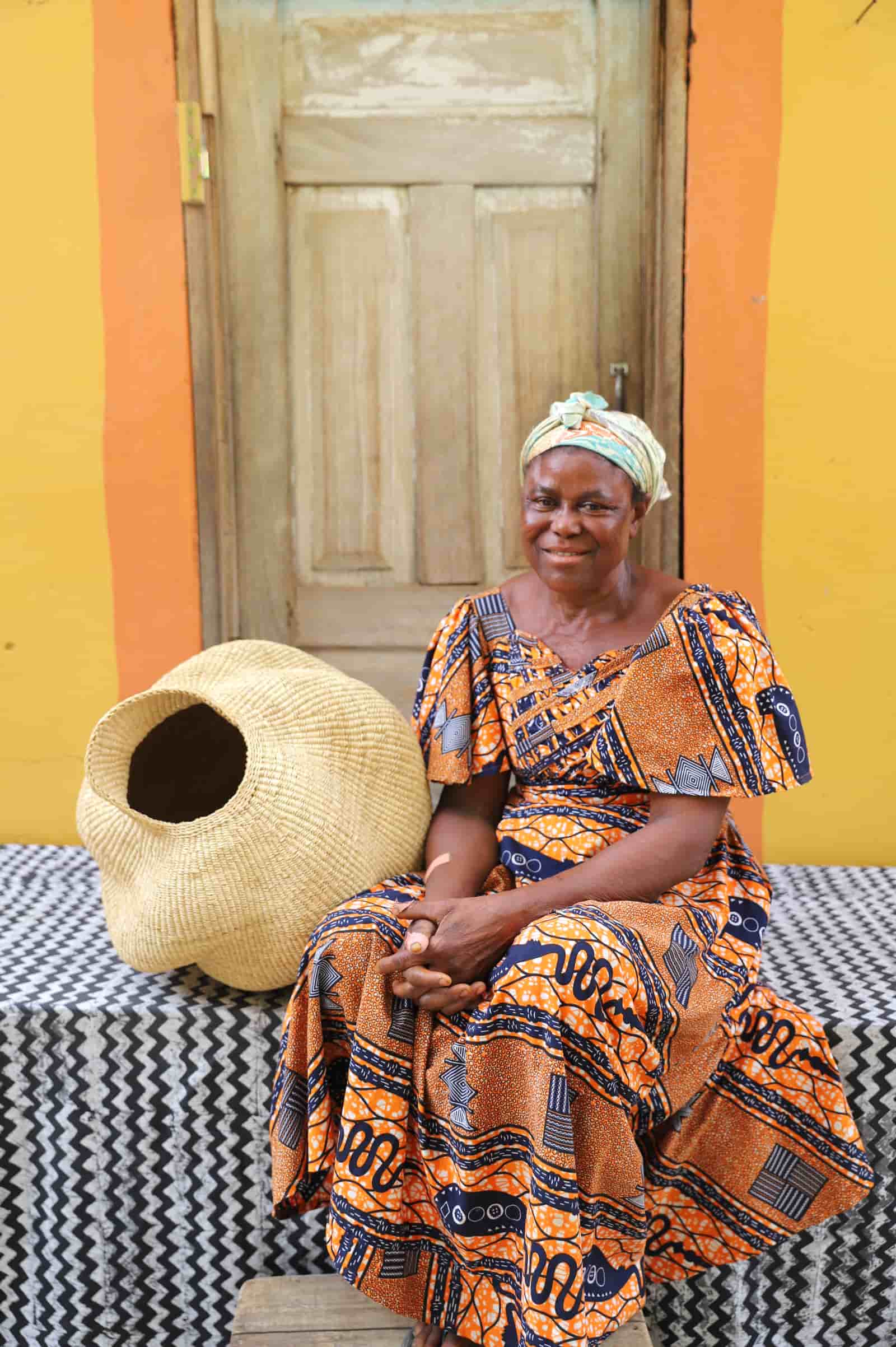 Woman sitting on a bench with a conch-shaped lampshade on a black and white cloth against a wooden door.