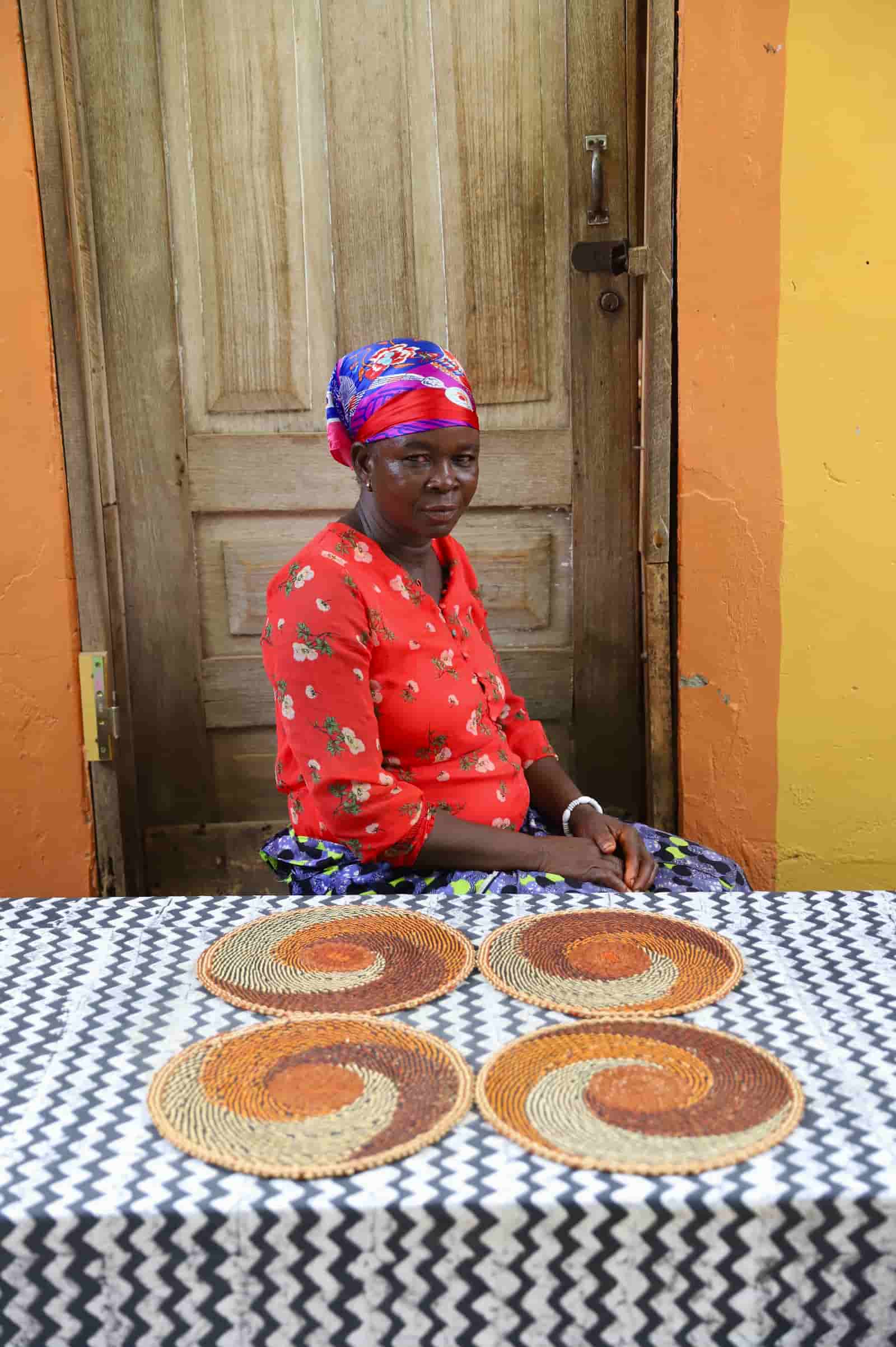 Artisan sitting with woven placemats on a black and white cloth against a wooden door.