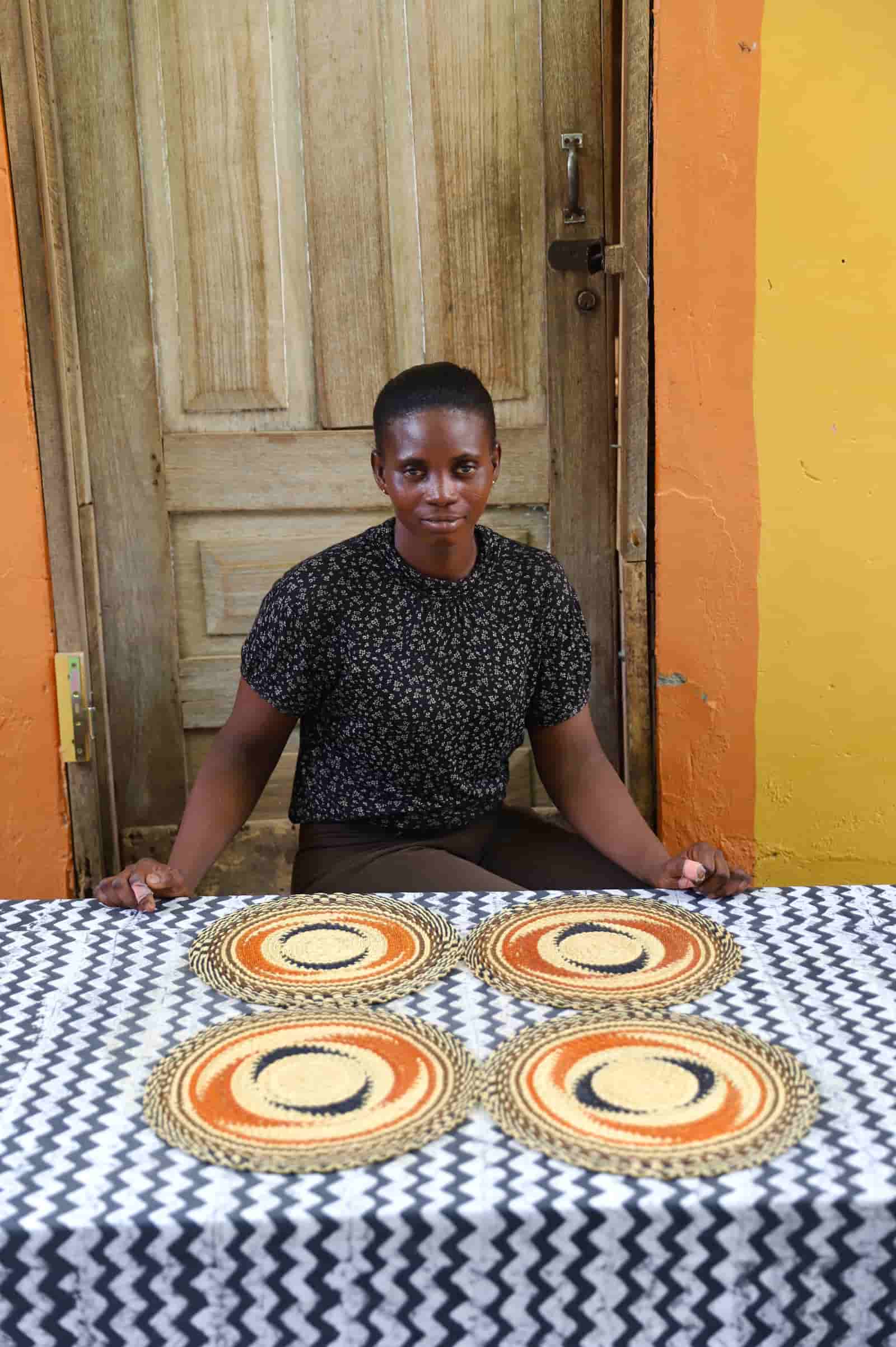 Artisan sitting with woven placemats on a black and white cloth against a wooden door.