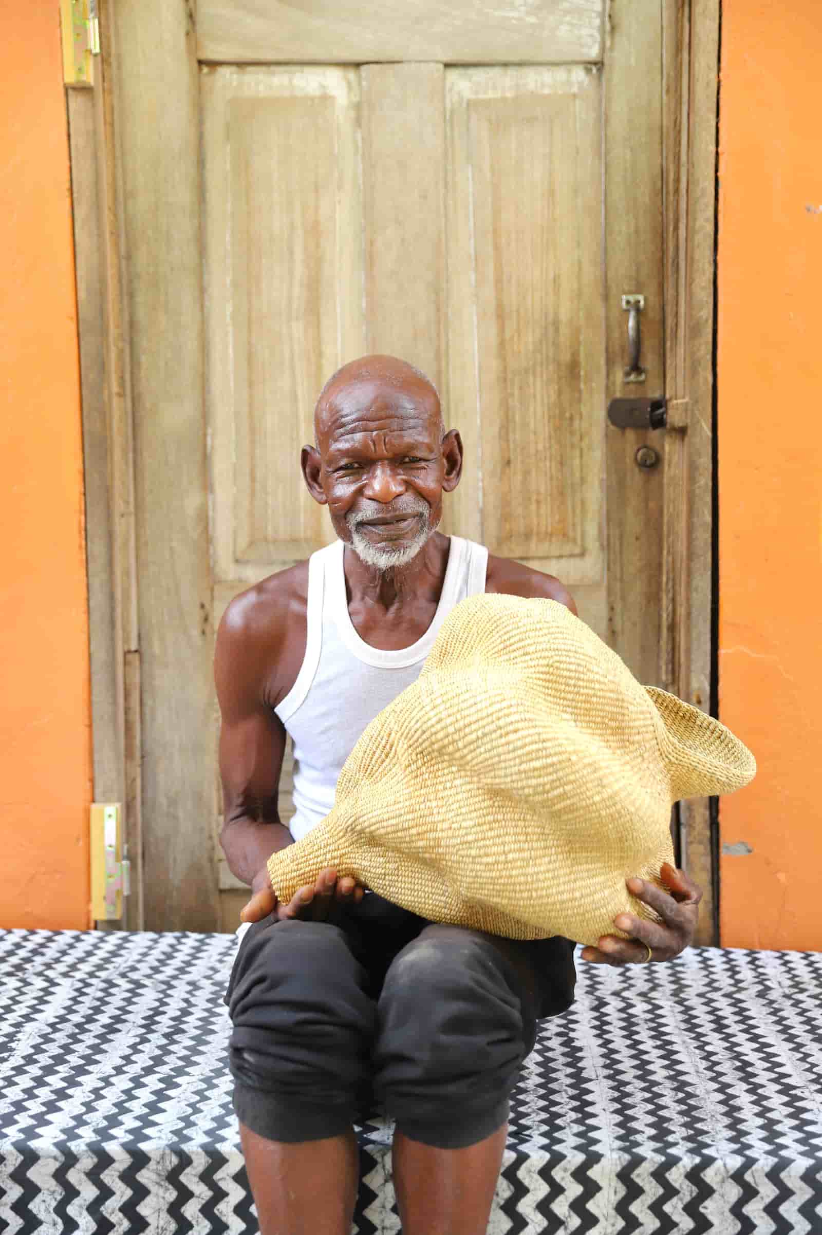 Man holding a woven conch-shaped lampshade on a black and white patterned cloth with a wooden door in the background.