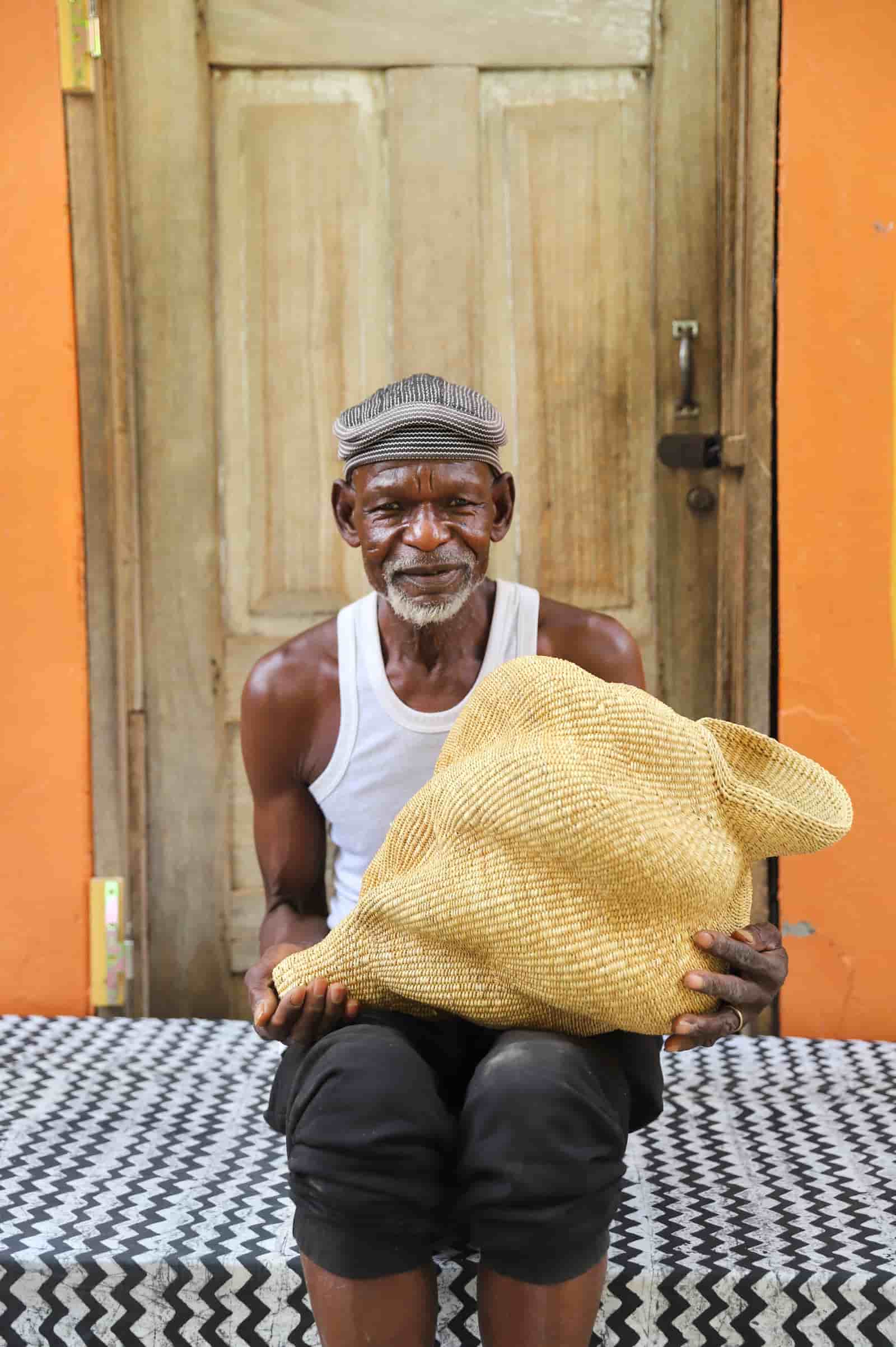 Man holding a woven conch-shaped lampshade on a black and white patterned cloth with a wooden door in the background.