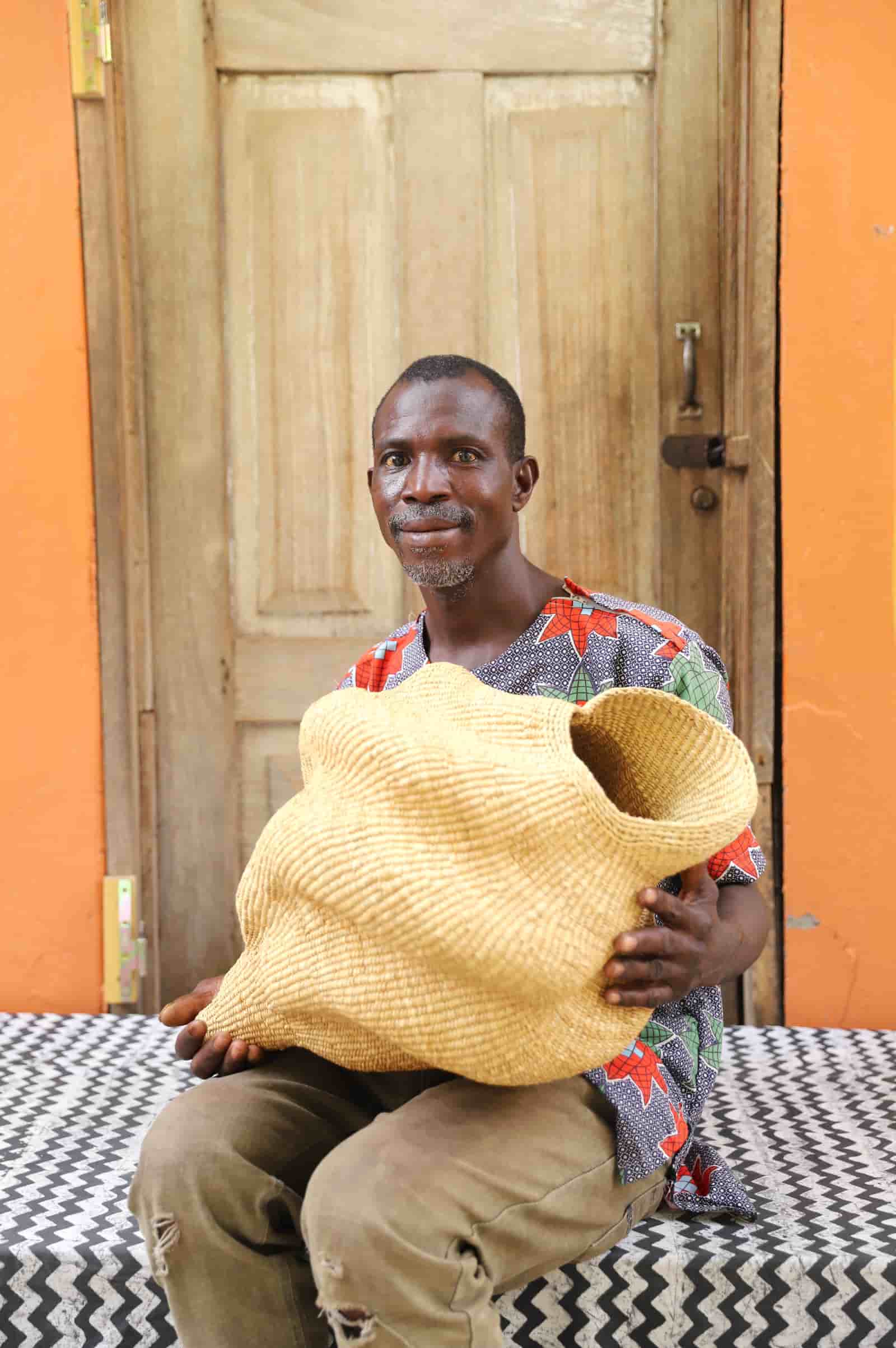 Man holding a large conch-shaped lampshade in front of a wooden door.