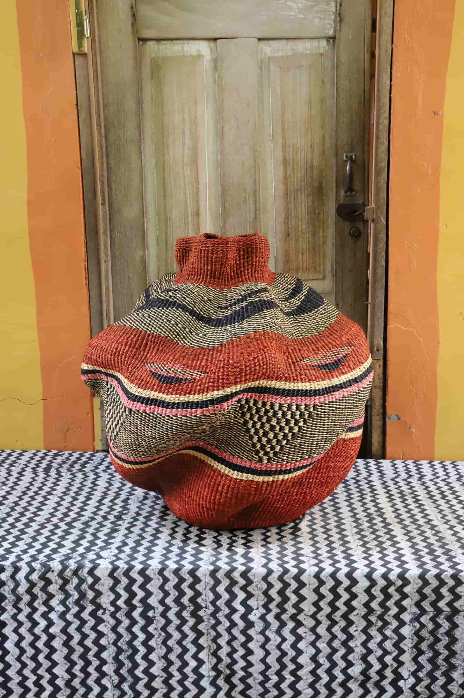 Large woven décor basket with colorful patterns on a black and white cloth with a wooden ndoor inn the background