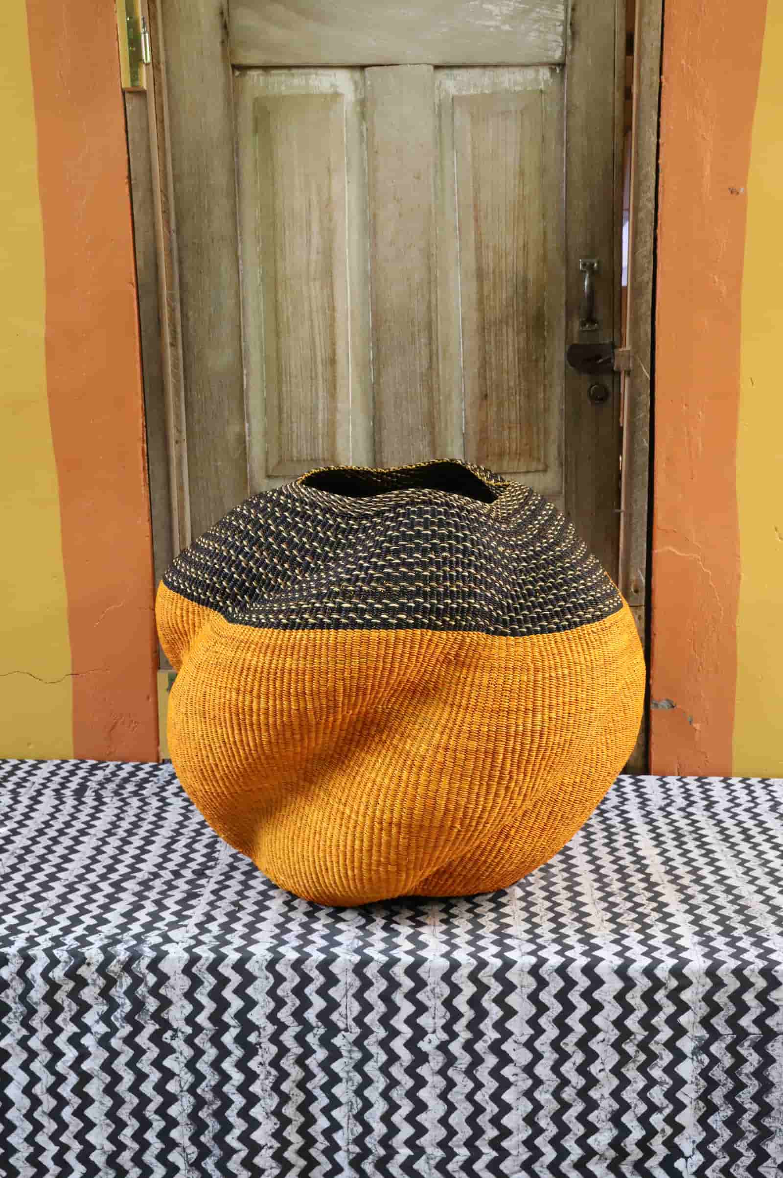 Handwoven Bolga basket in amber with a dark striped collar, on a black and white chevron cloth before a wooden door.