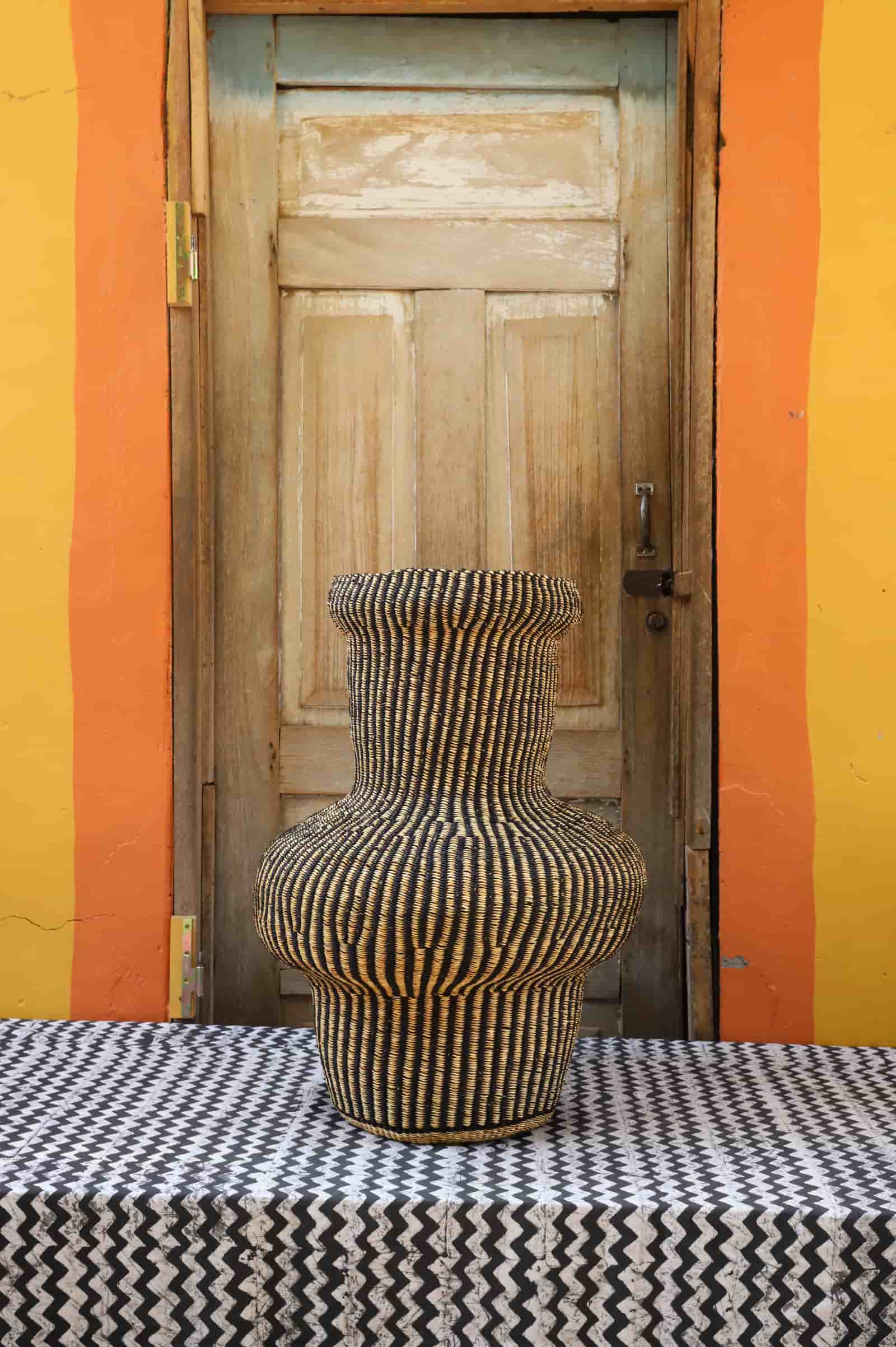 Colorful woven piece on a black and white patterned surface with a wooden door in the background.