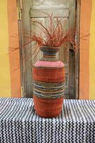 Decorative woven vase with red branches on a tablecloth against a colorful wall.