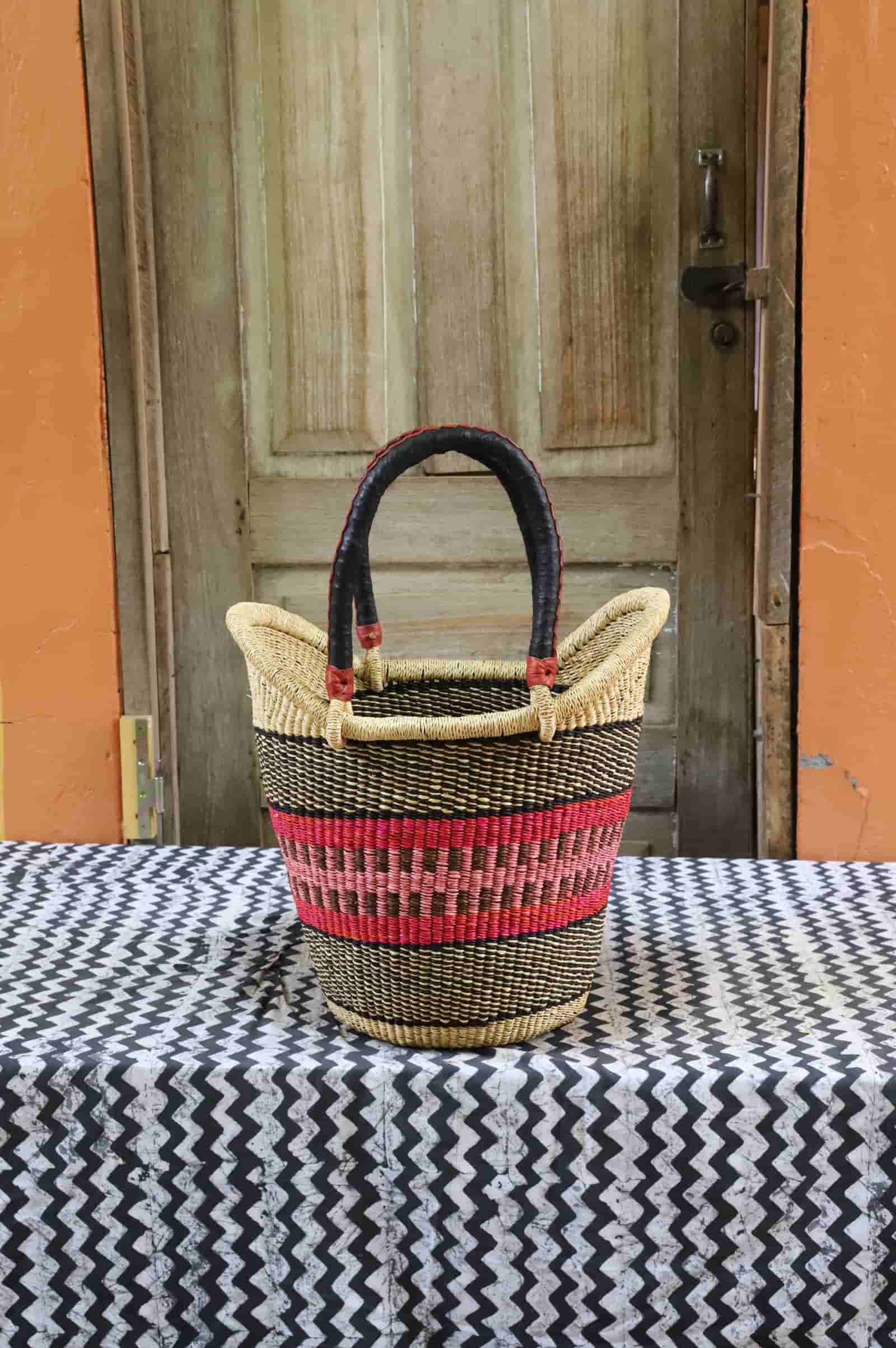 Colorful woven carry on bag with premium leather handles on a black and white cloth against a wooden door.