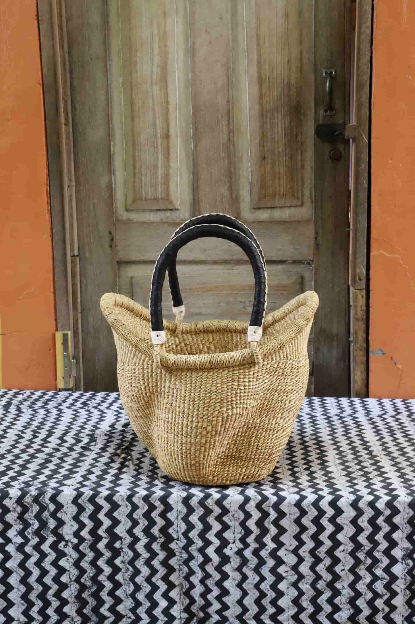 Woven basket with black handles on a tablecloth in front of a wooden door.