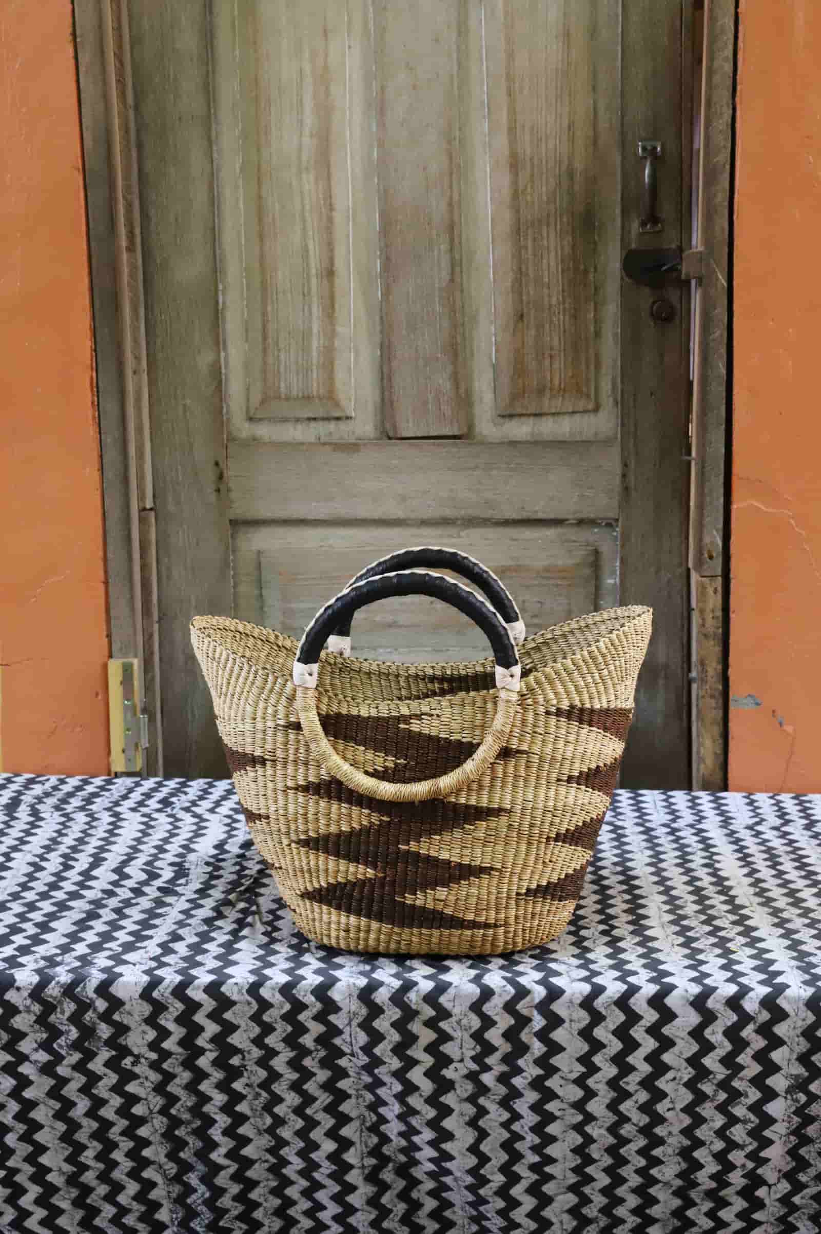 Woven basket with black and beige handle on a tablecloth in front of a wooden door.
